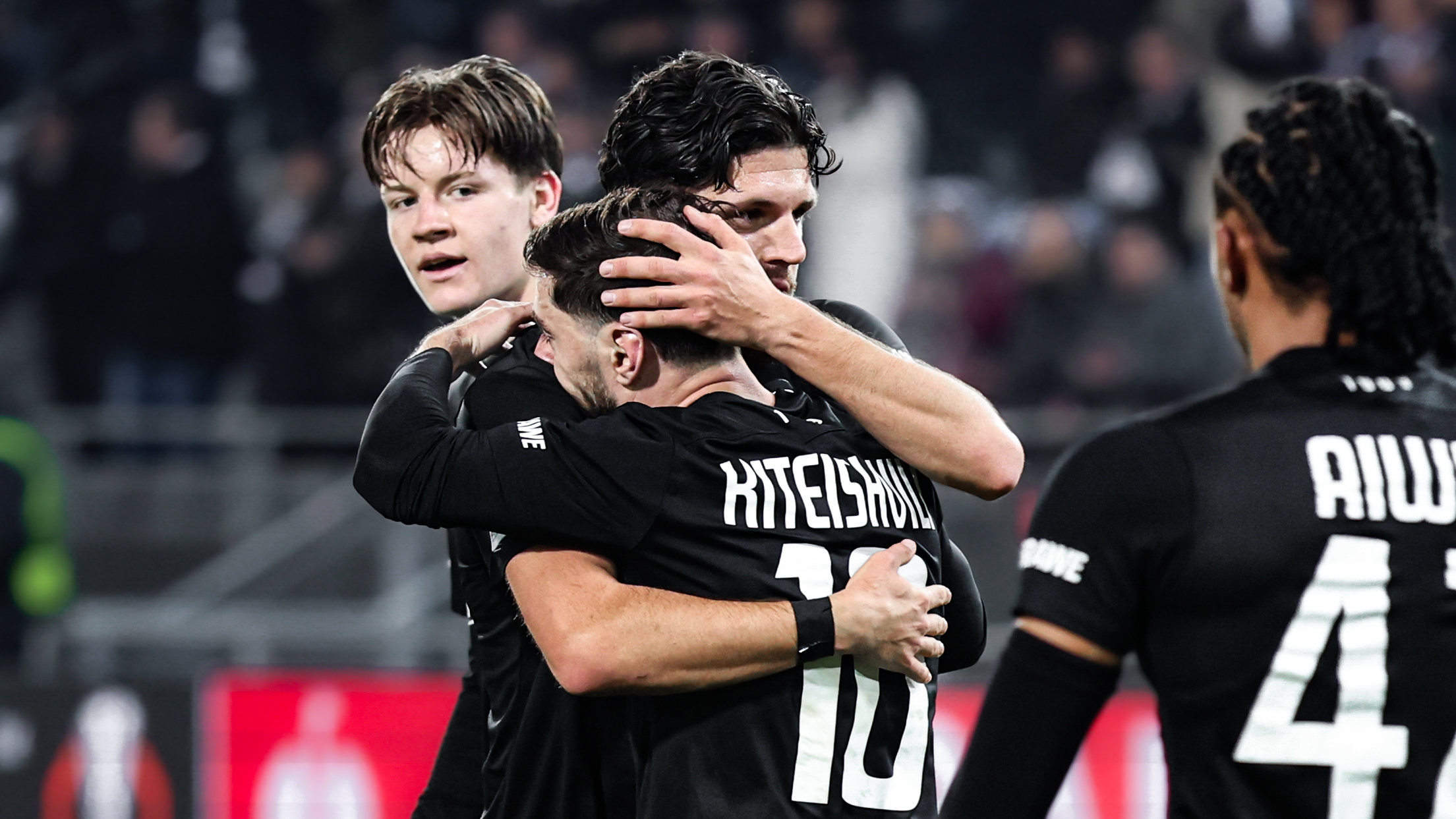 Vier Spieler in schwarzen Trikots jubeln und liegen sich in den Armen