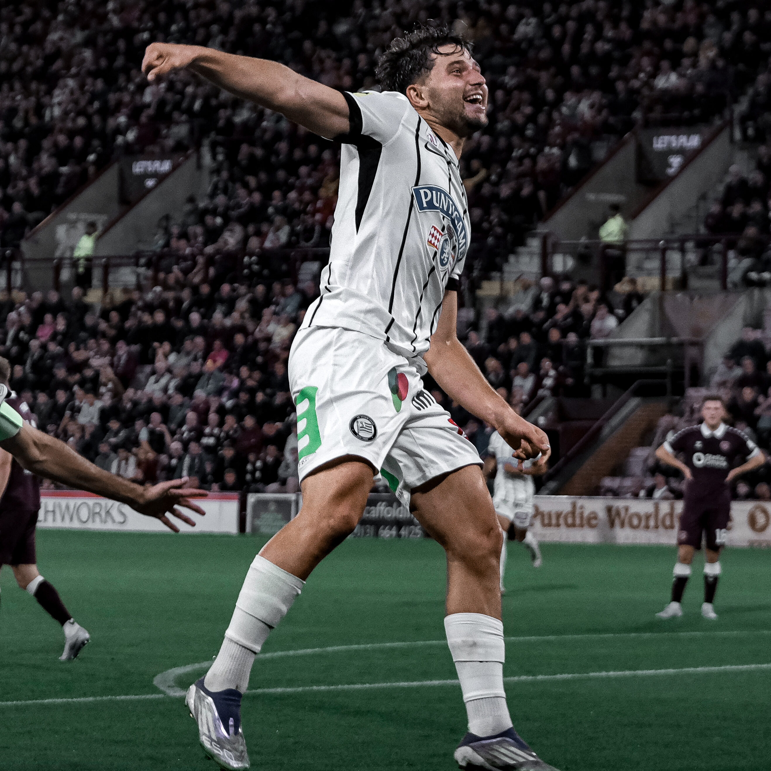 Ein Spieler in einem weißen Trikot springt, streckt die Arme weg und lacht.