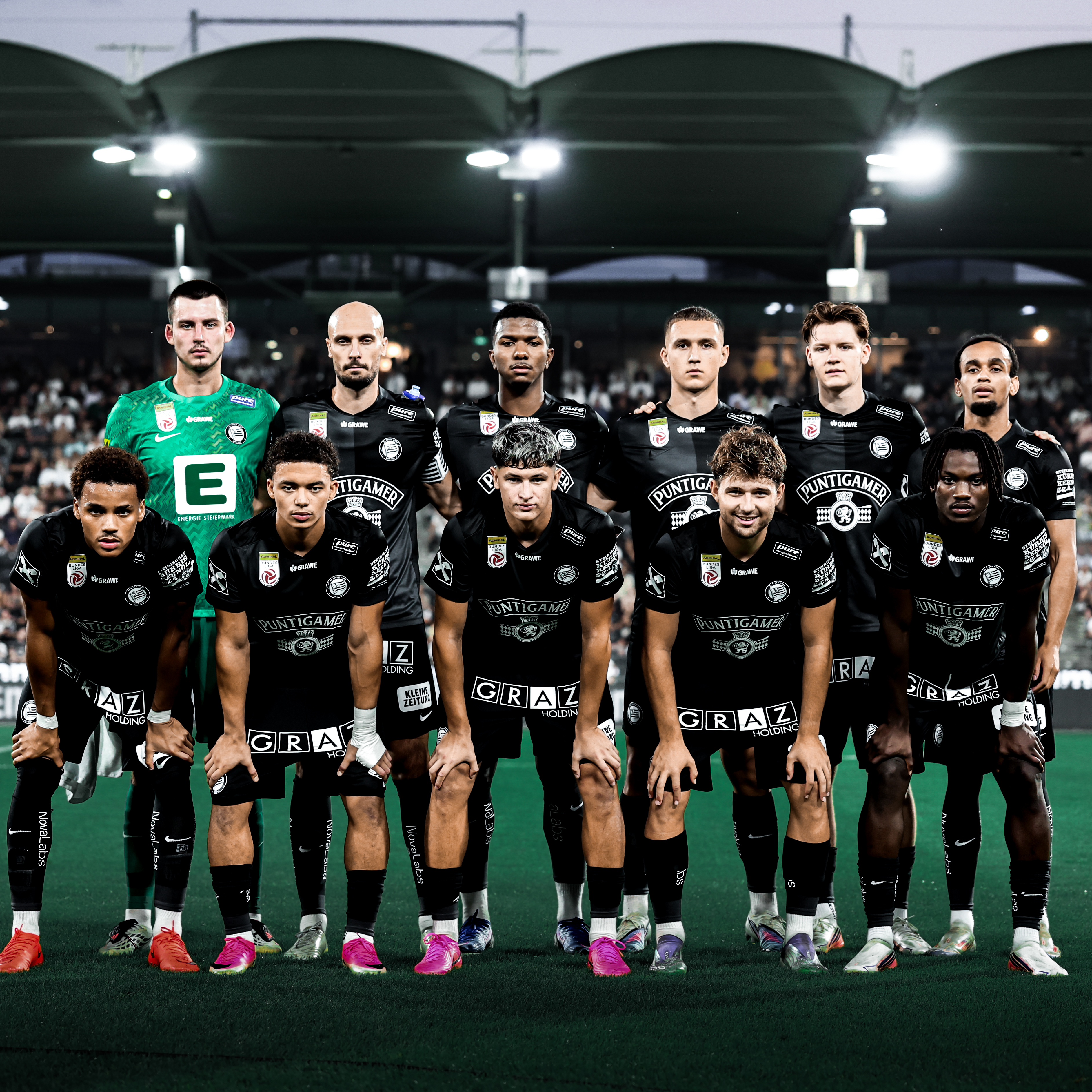 Elf Spieler in schwarz stehen in zwei Reihen und schauen in die Kamera