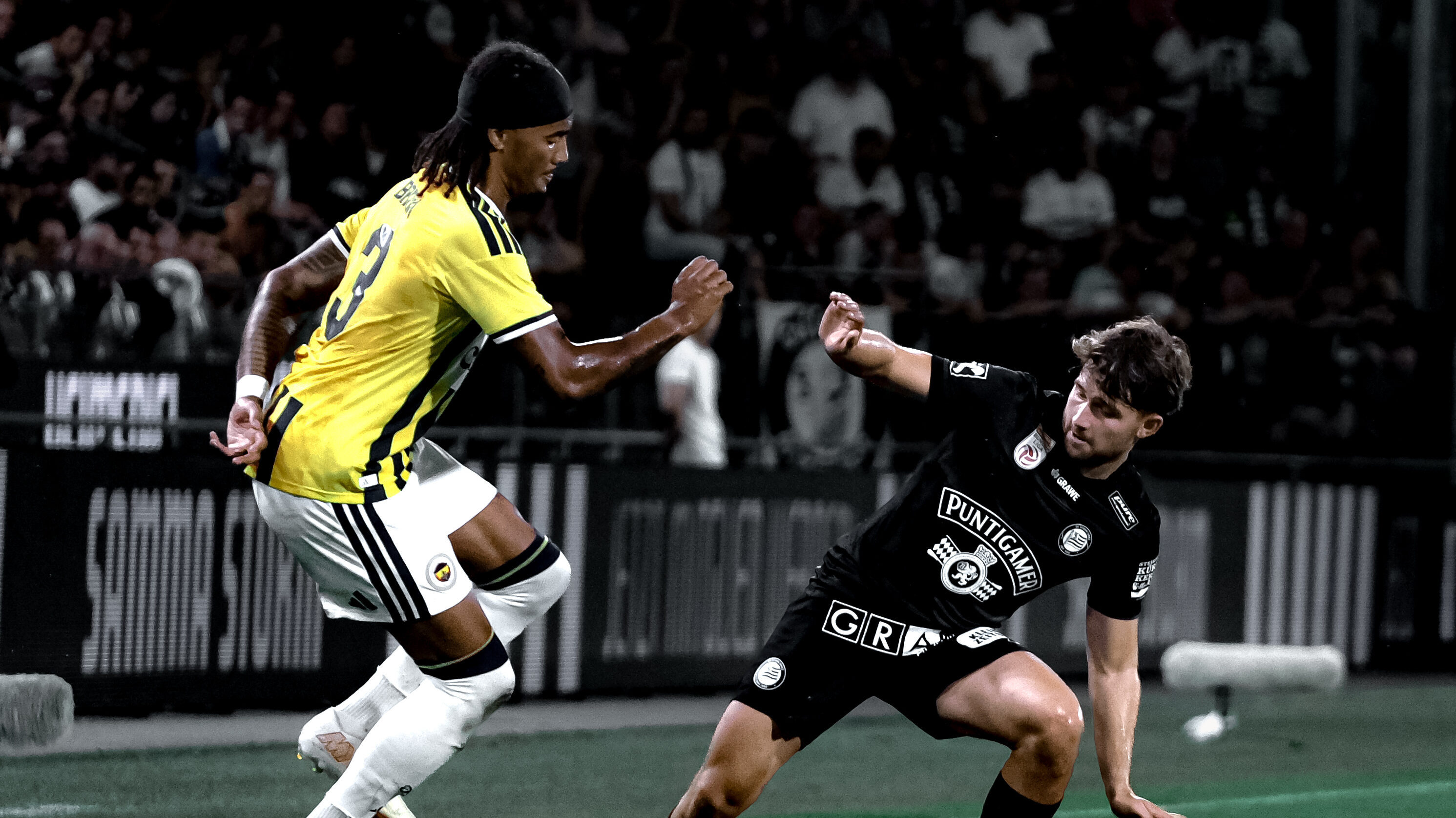 Ein Spieler in gelb-blau und ein Spieler in schwarz kämpfen um einen weißen Ball.