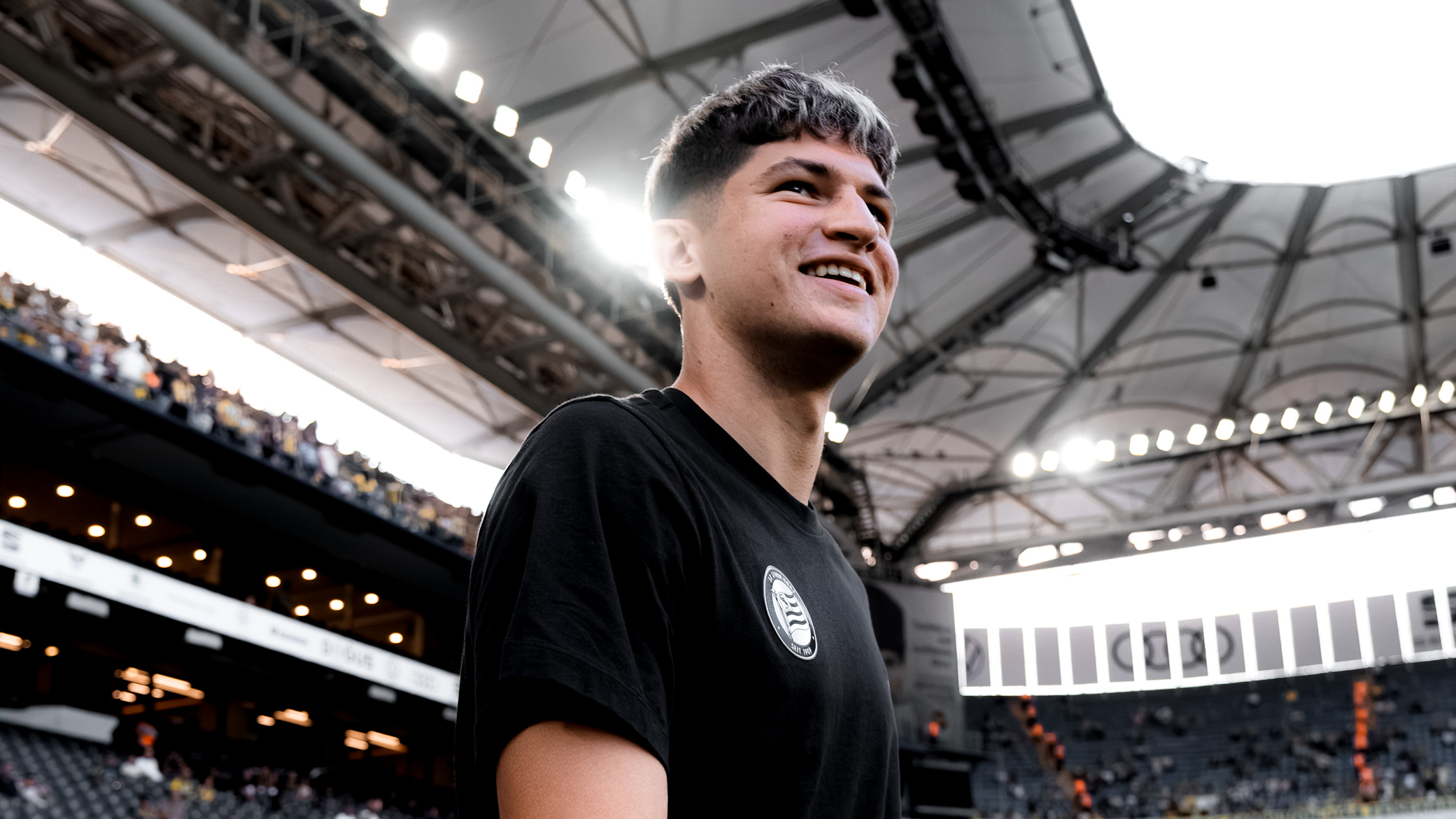 Ein Spieler betritt lachend ein Stadion.