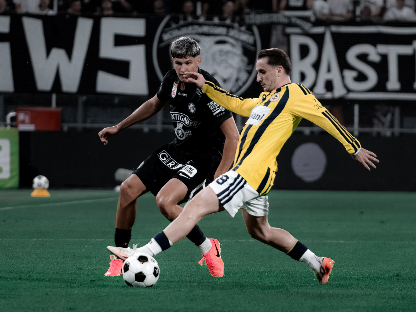 Ein Spieler in gelb-blau und ein Spieler in schwarz kämpfen um einen weißen Ball.