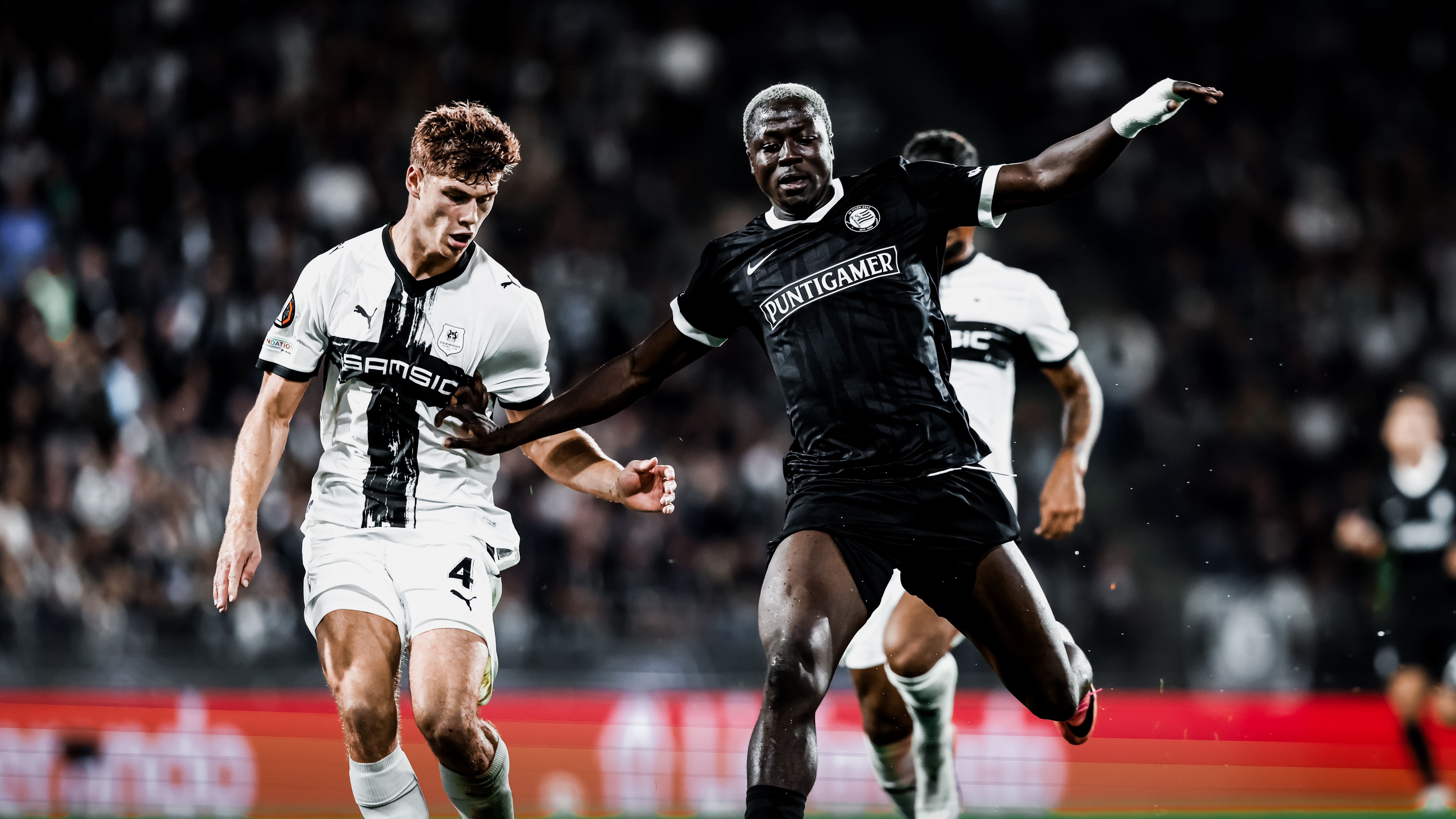 Ein Spieler in einem schwarzen Trikot und ein Spieler in einem weißen Trikot kämpfen um einen Ball.