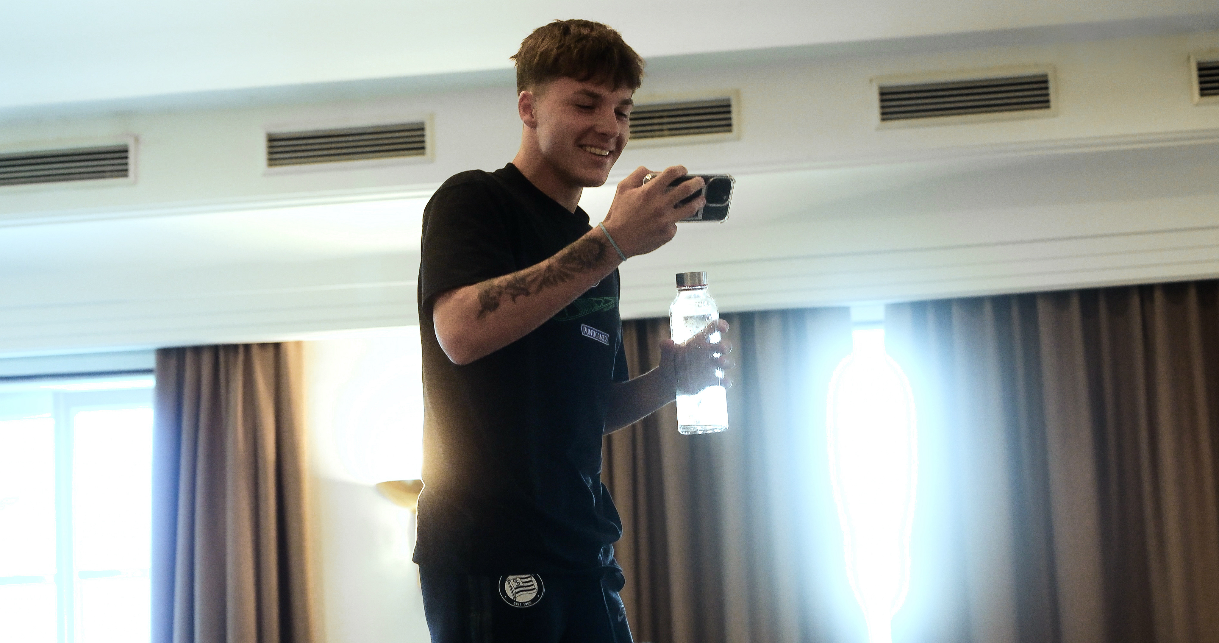 Ein Mann lachend mit Handy und Flasche