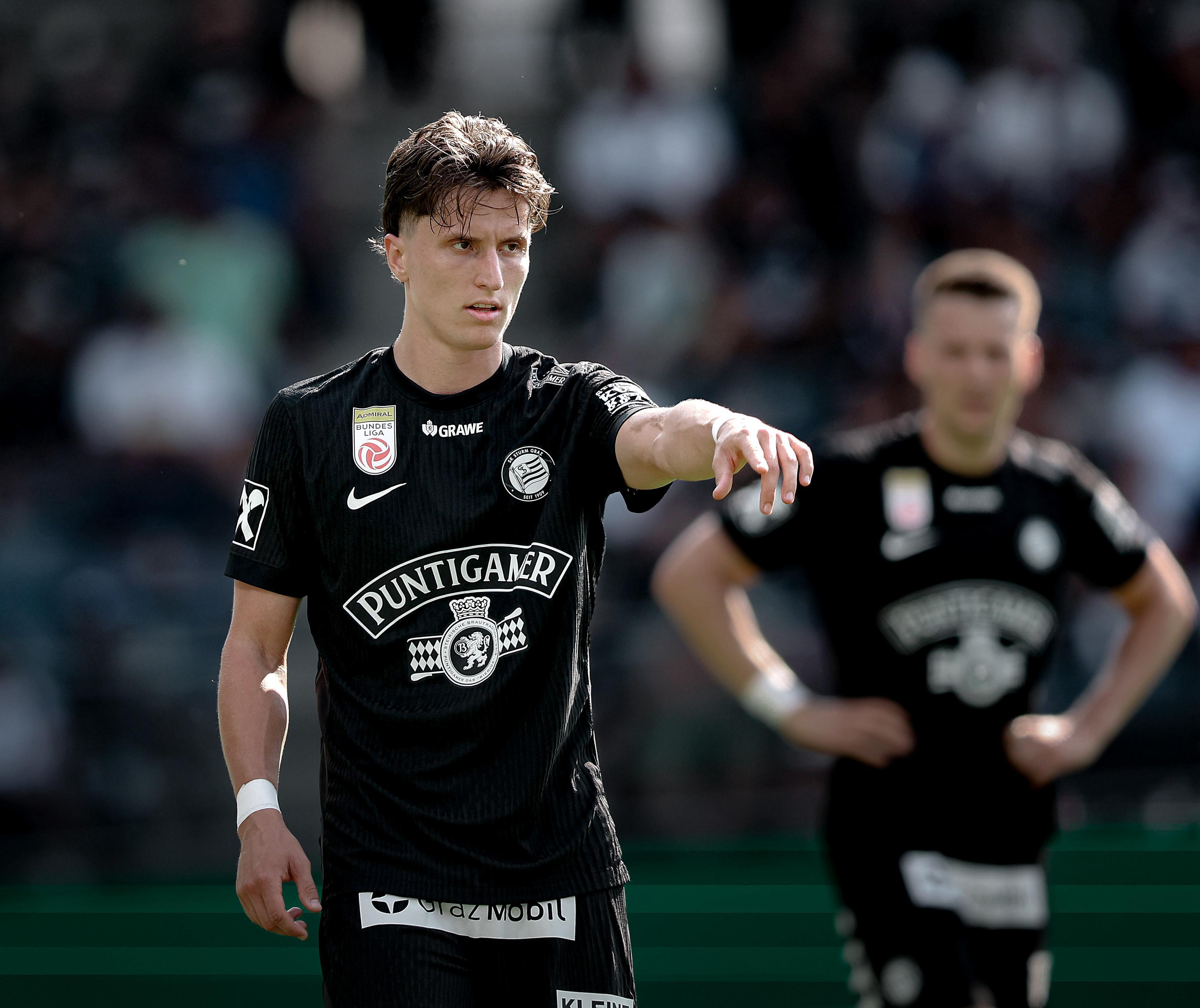 Zwei Fußballer stehen in schwarzen Trikots am Feld.