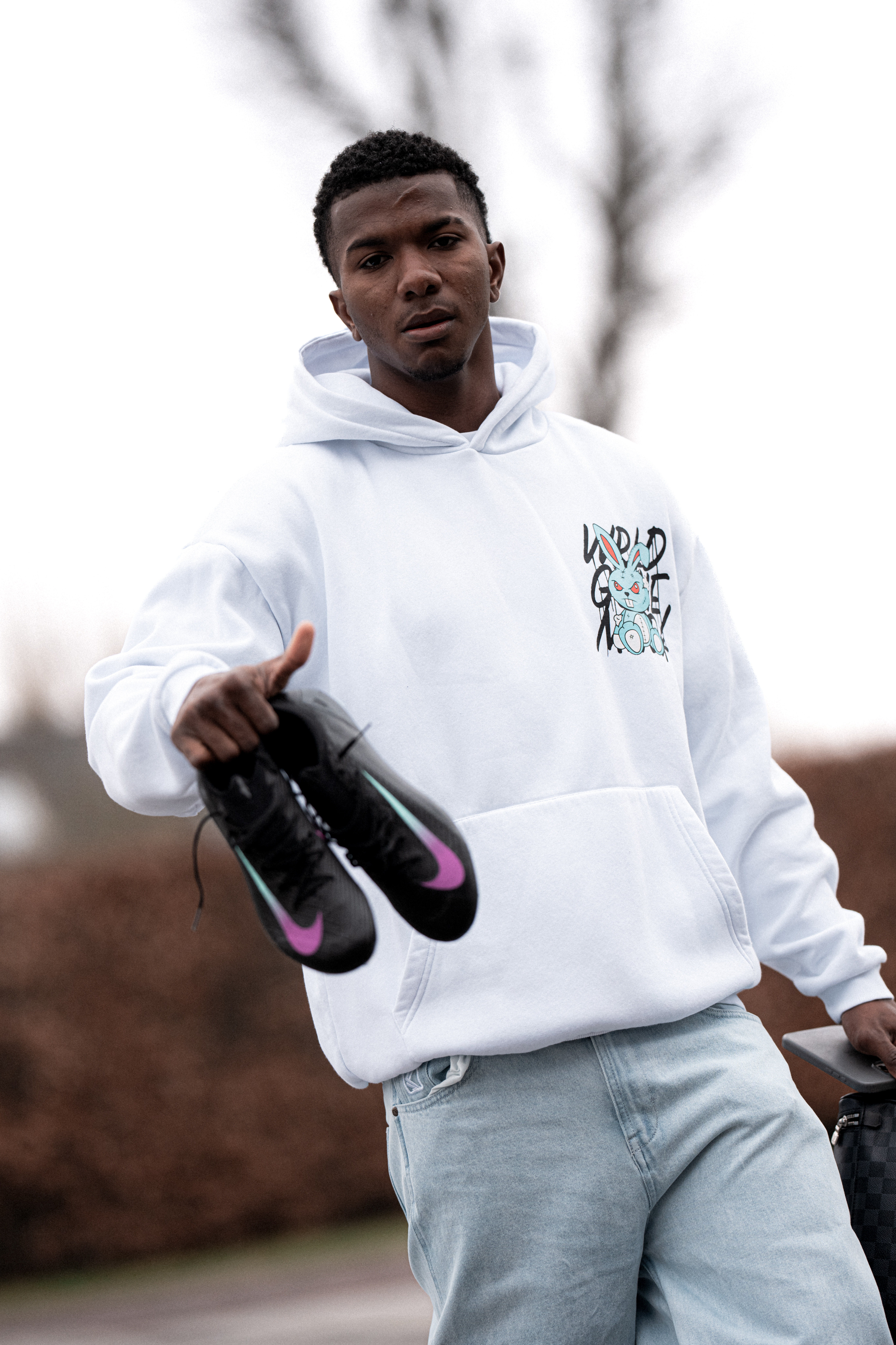 MAnn in Hoody hält Fußballschuhe in die Kamera