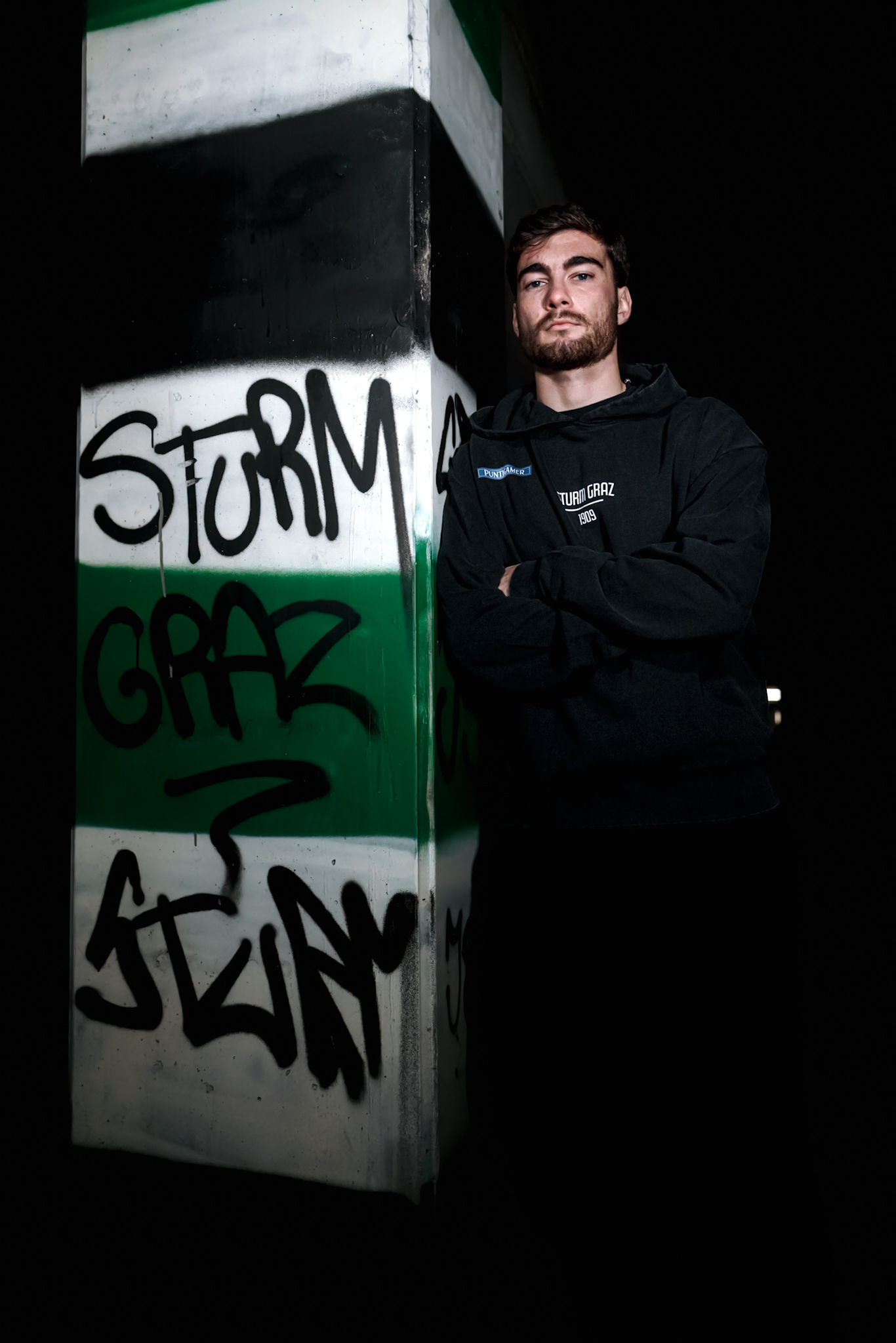 Mann lehnt an Säule die mit Graffiti vollgesprüht ist.