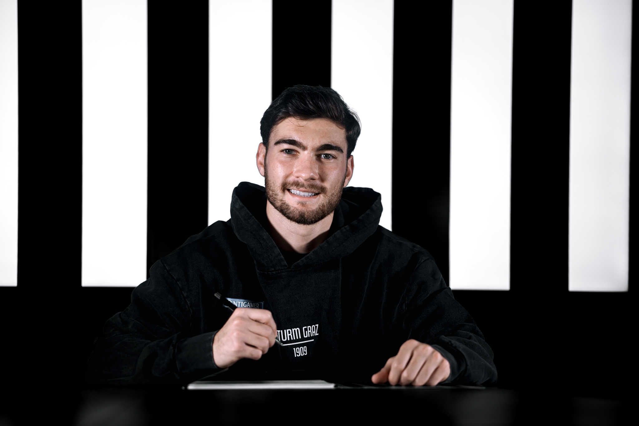 Mann schreibt auf einem Blatt Papier vor einem schwarz-weißem Hintergrund.