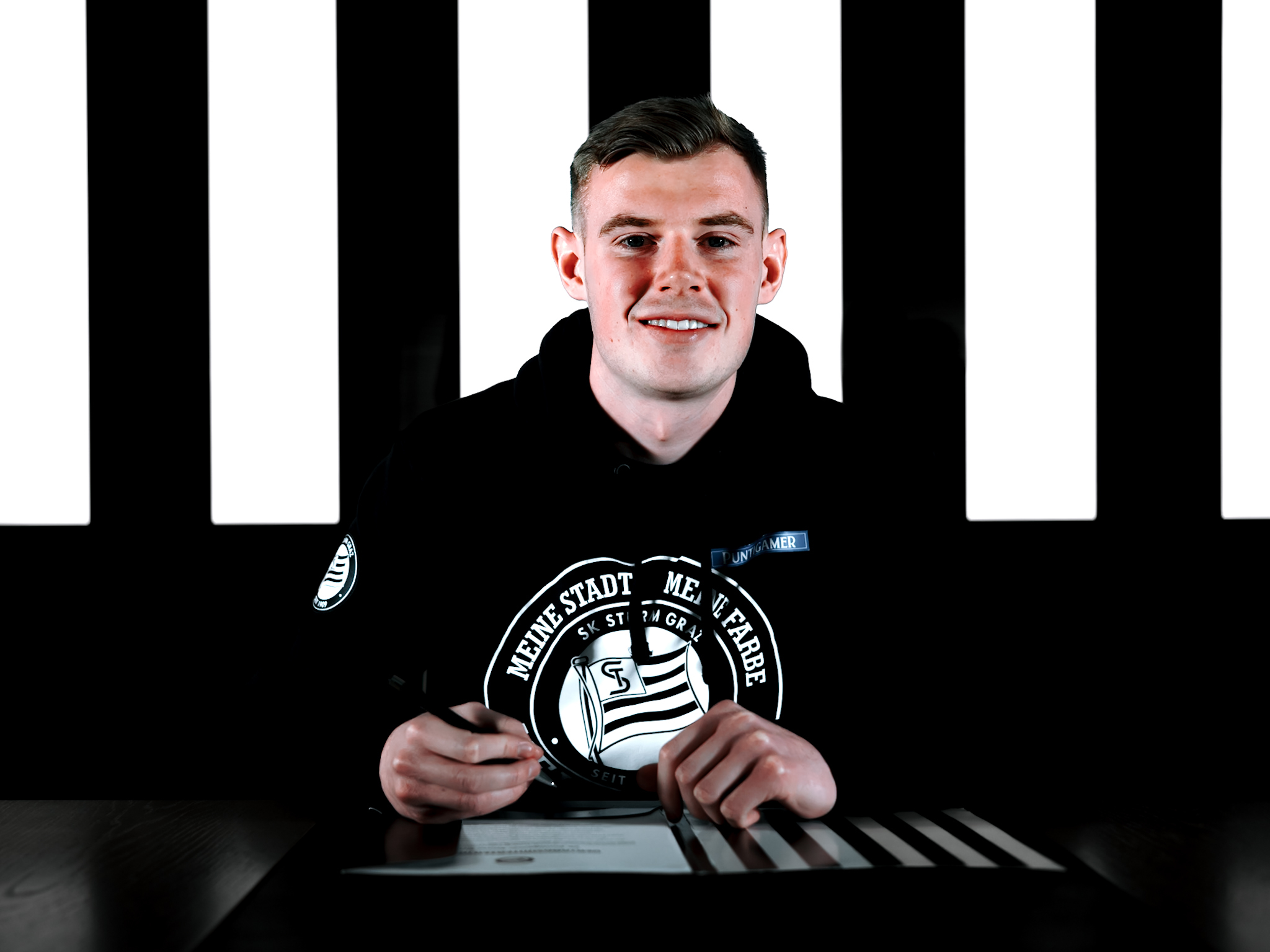 Man unterschreibt auf Papier vor einer schwarz-weißen Wand.