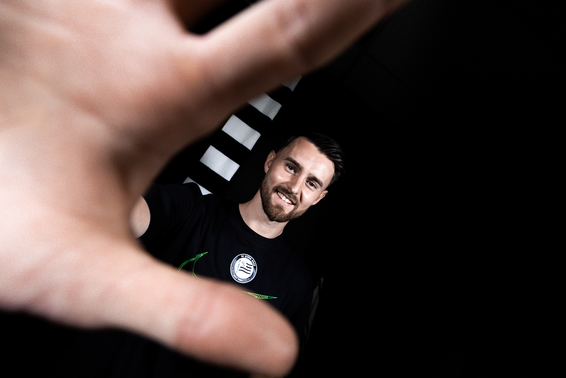 Mann in schwarzem Shirt streckt die Hand nach der Kamera.