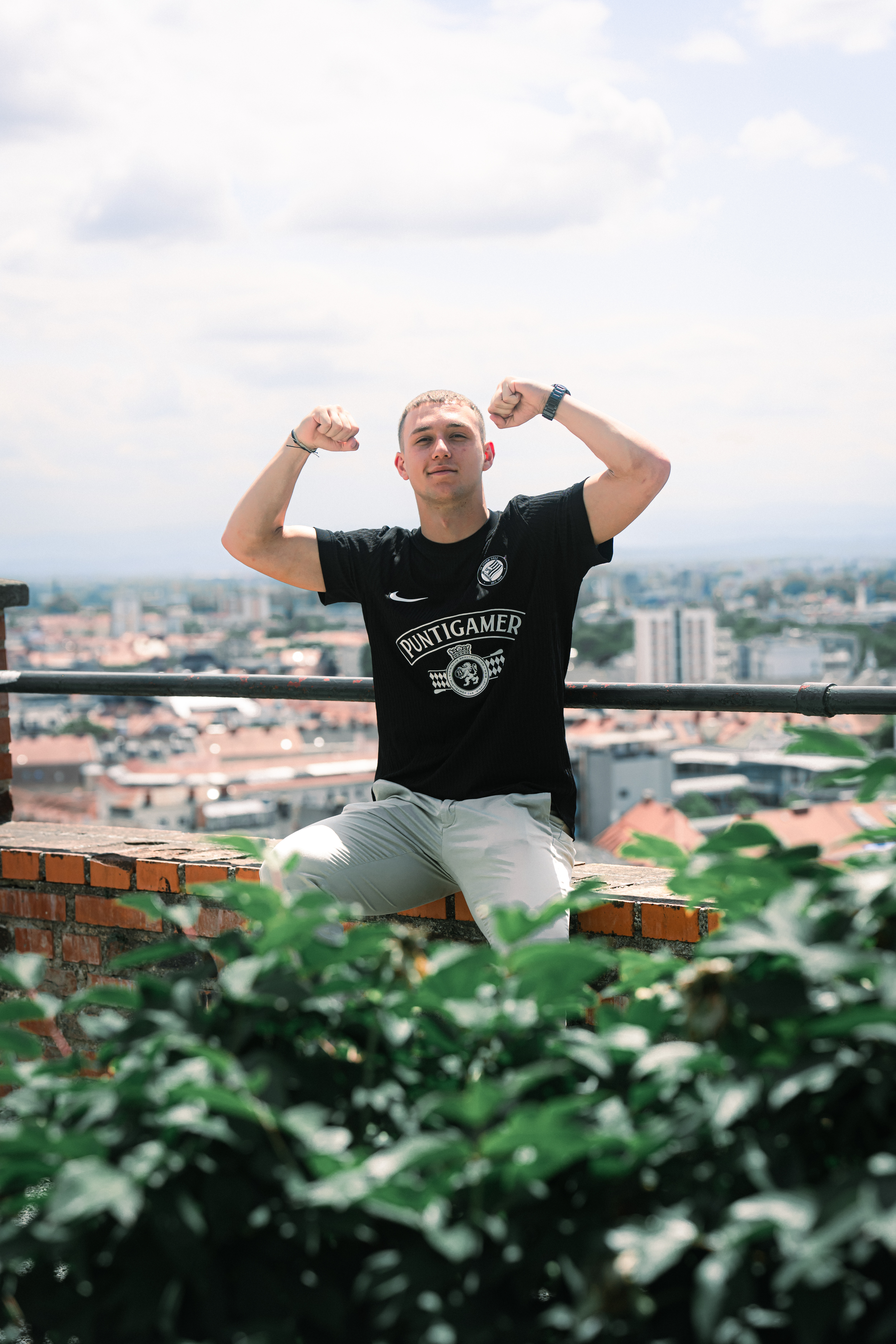 Mann mit Muskelpose sitzt auf einer Mauer.