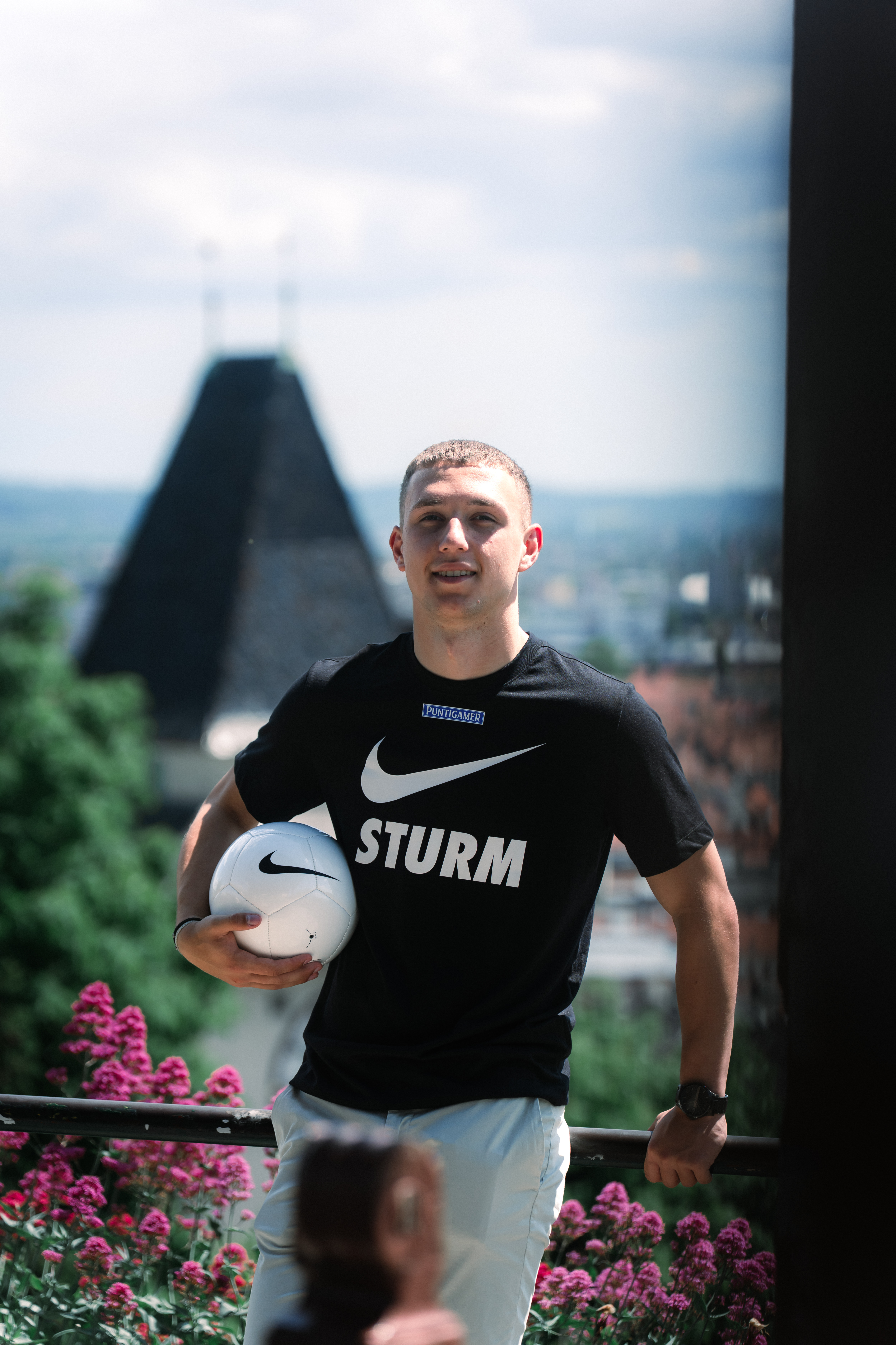 Mann mit Ball unter dem Arm steht vor dem Grazer Uhrturm.