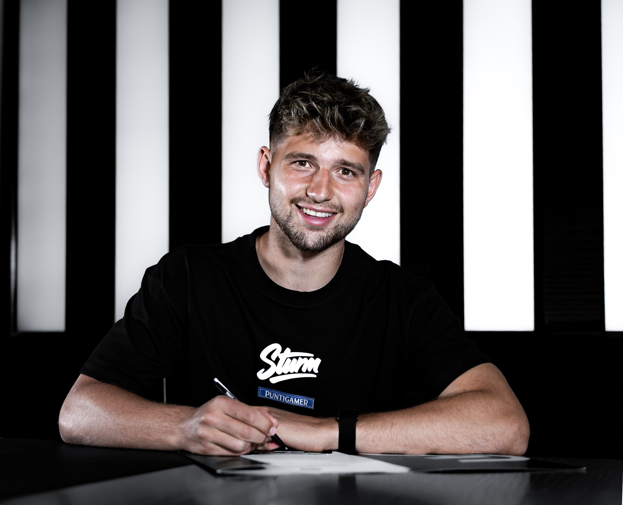 Mann in schwarzem Shirt unterschreibt ein Papier.