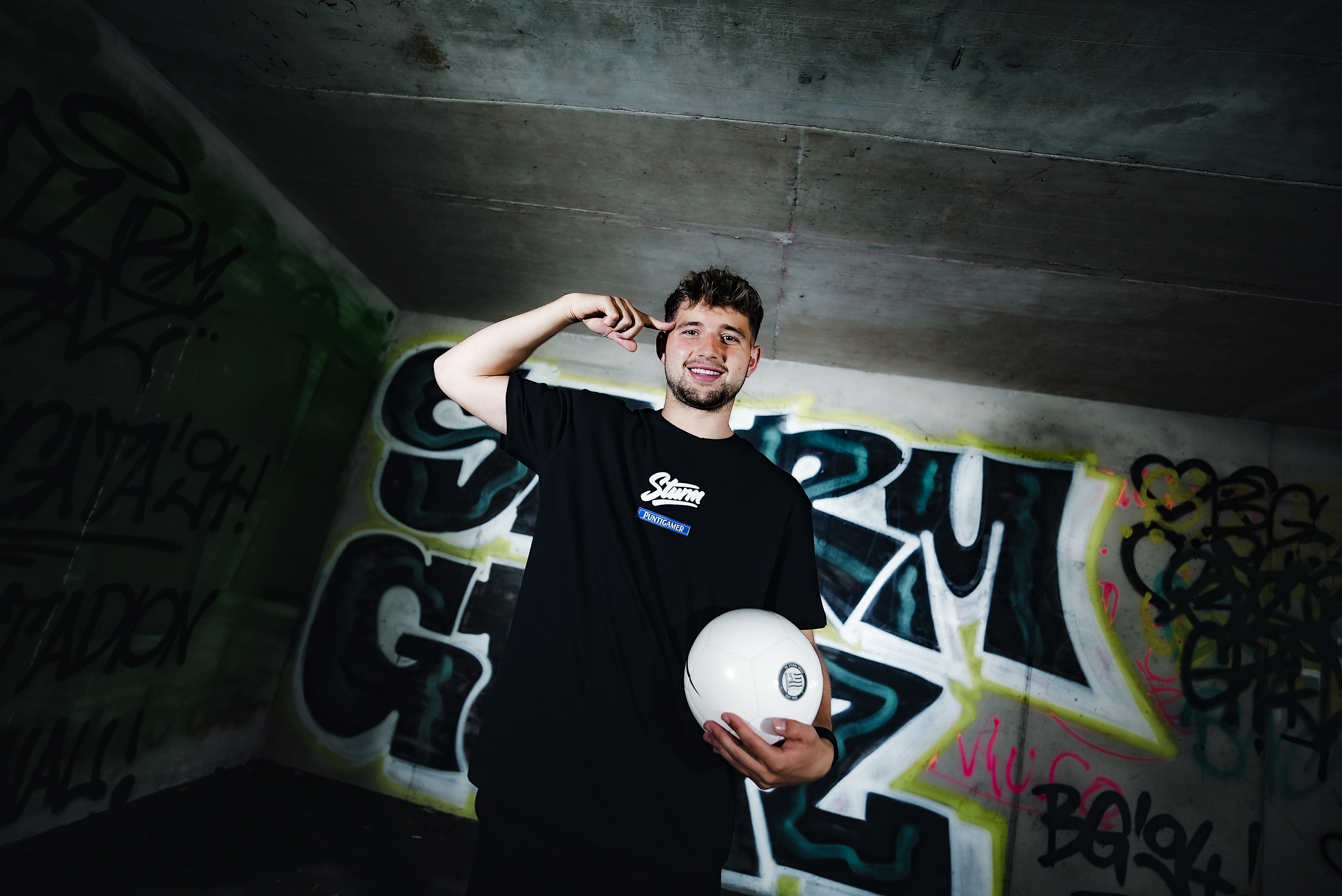 Mann steht vor einem Grafiti und hält einen weißen Ball.