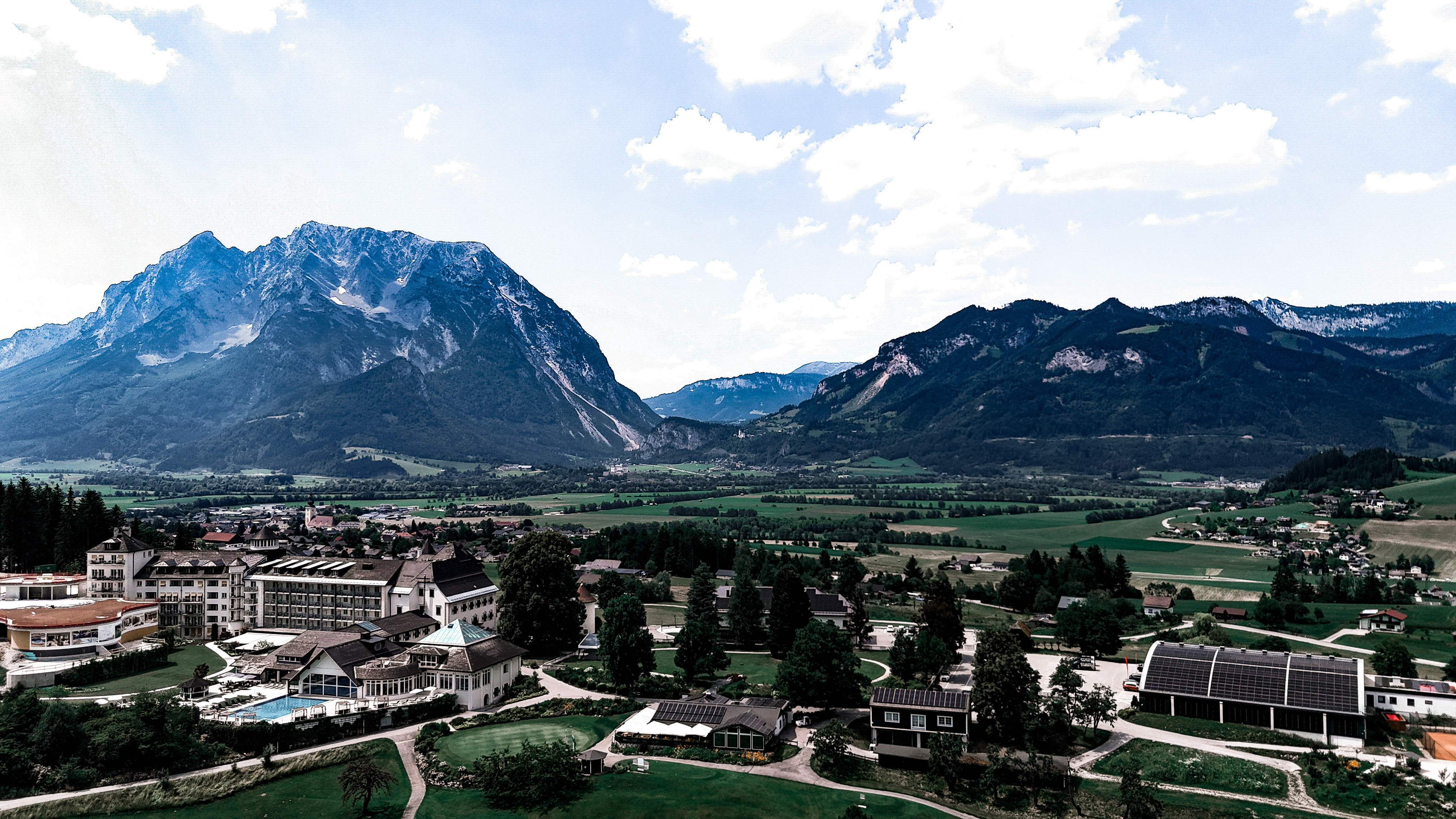 Luftaufnahme von einem Schloß mit Golfplatz daneben und einem Berg im Hintergrund.