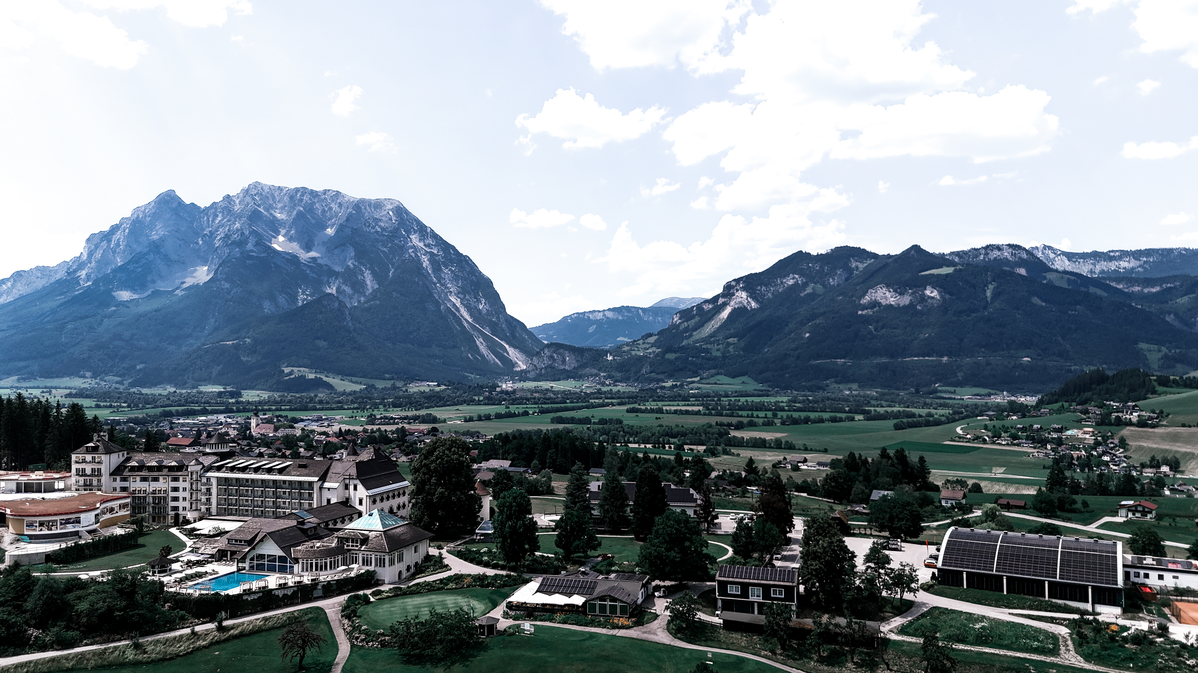 Luftaufnahme von einem Schloß mit Golfplatz daneben und einem Berg im Hintergrund.