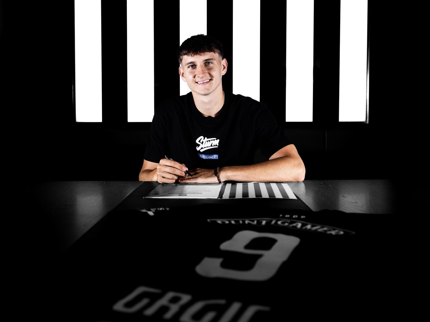 Junger Mann unterschreibt einen Vertrag, vor ihm liegt ein schwarzes Trikot.