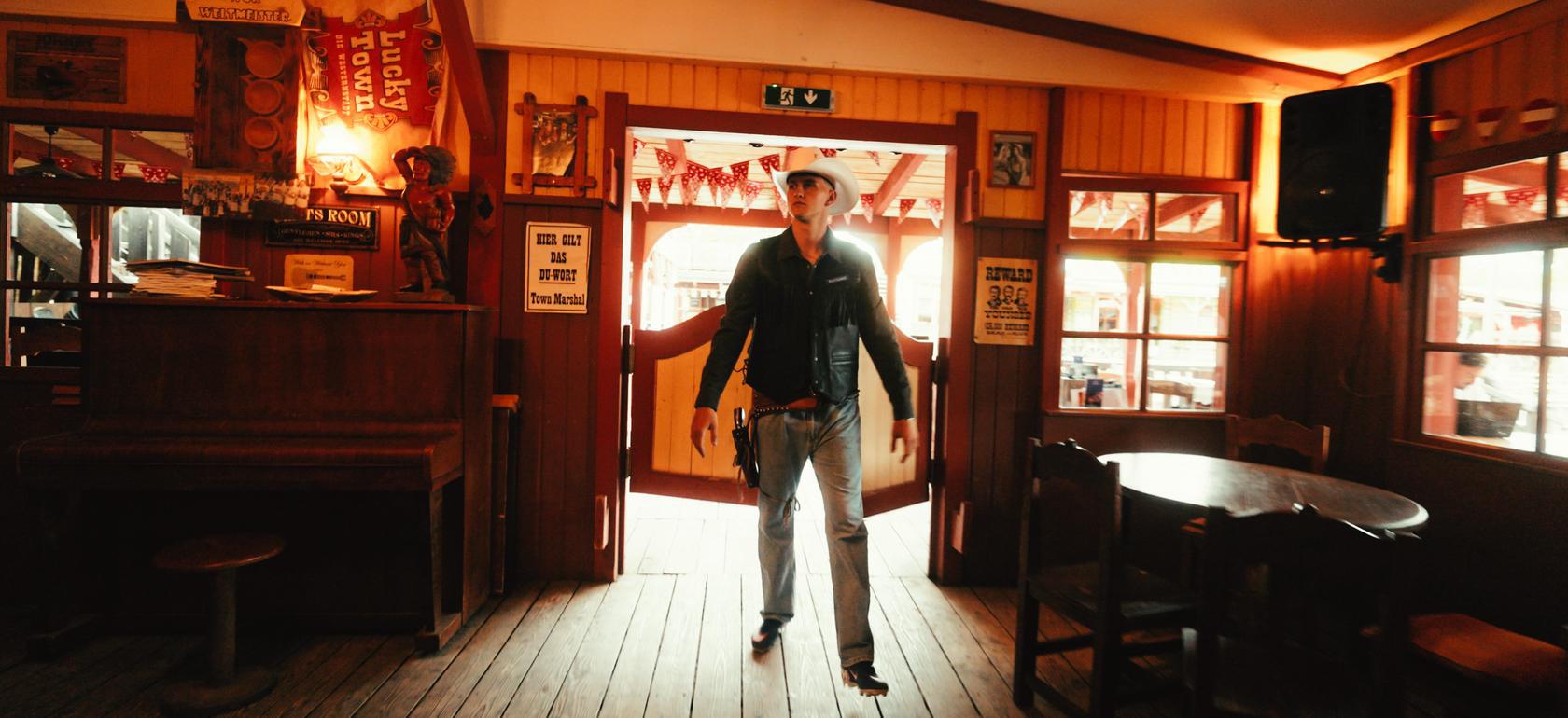 Mann in Cowboy-Outfit steht in einem Saloon.