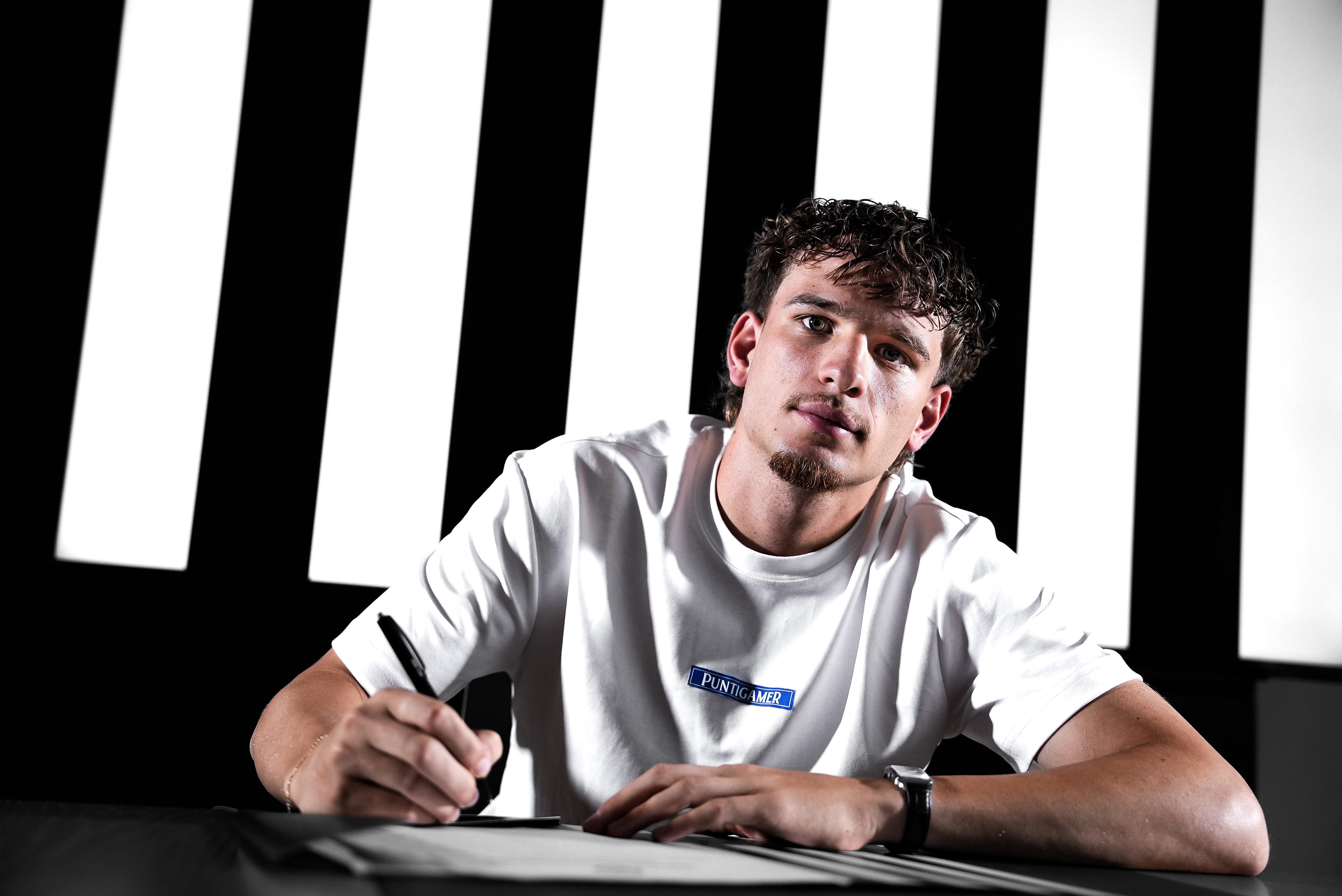 Junger man in weißem Shirt unterschreibt ein Blatt Papier.