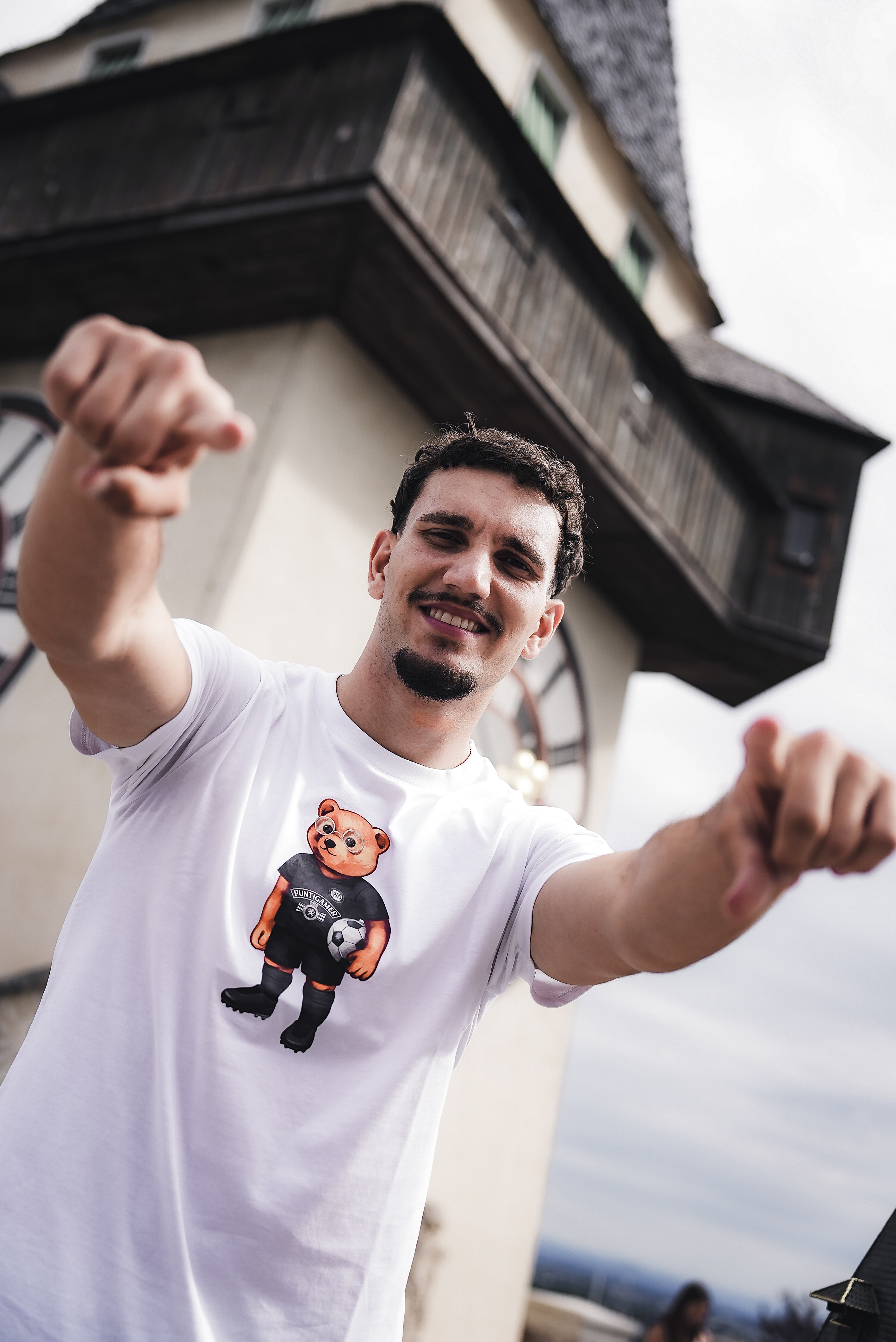 Eine Person steht vor dem Uhrturm und zeigt mit beide Zeigefinger zur Kamera