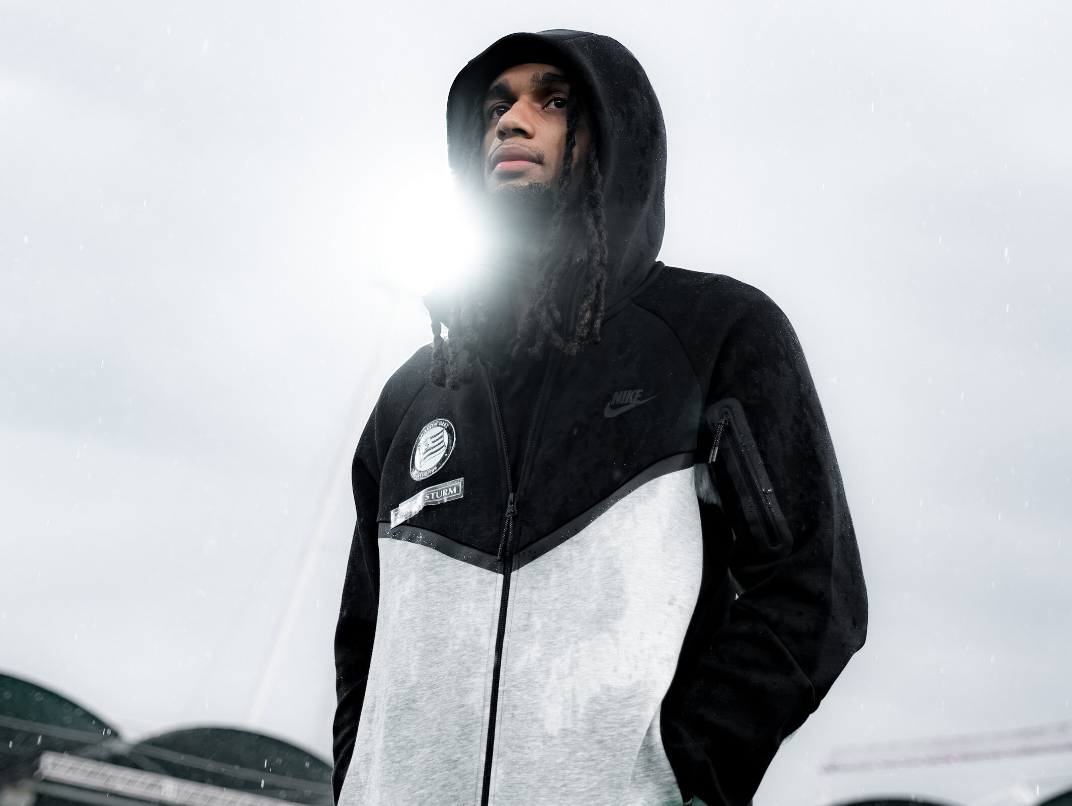 Mann mit grau-schwarzem Hoodie hat die Hände in den Taschen.