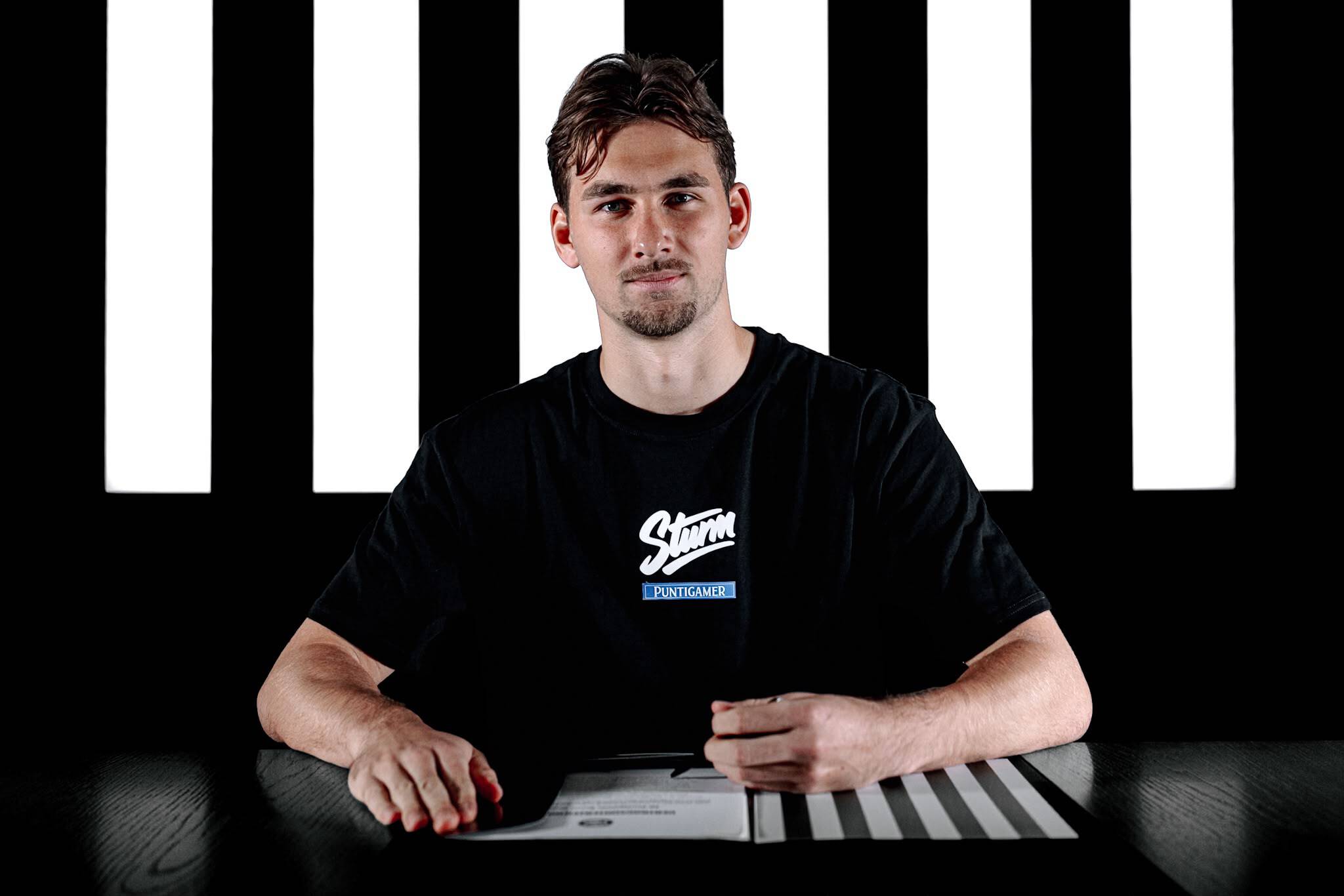 Junger Mann in schwarzem Shirt unterschreibt ein Papier.