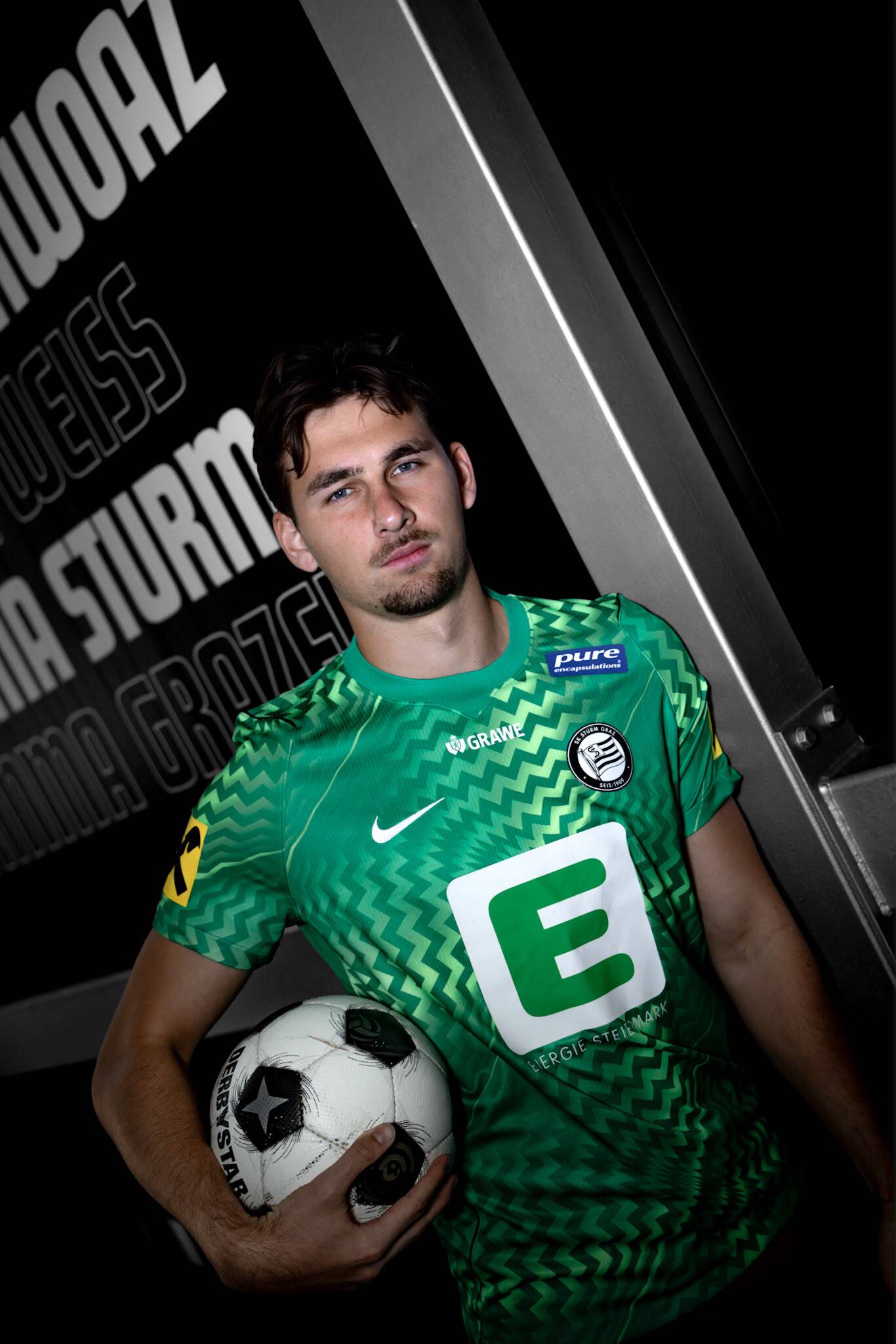 Mann in grünem Fußballtrikot hält Ball unter dem Arm.