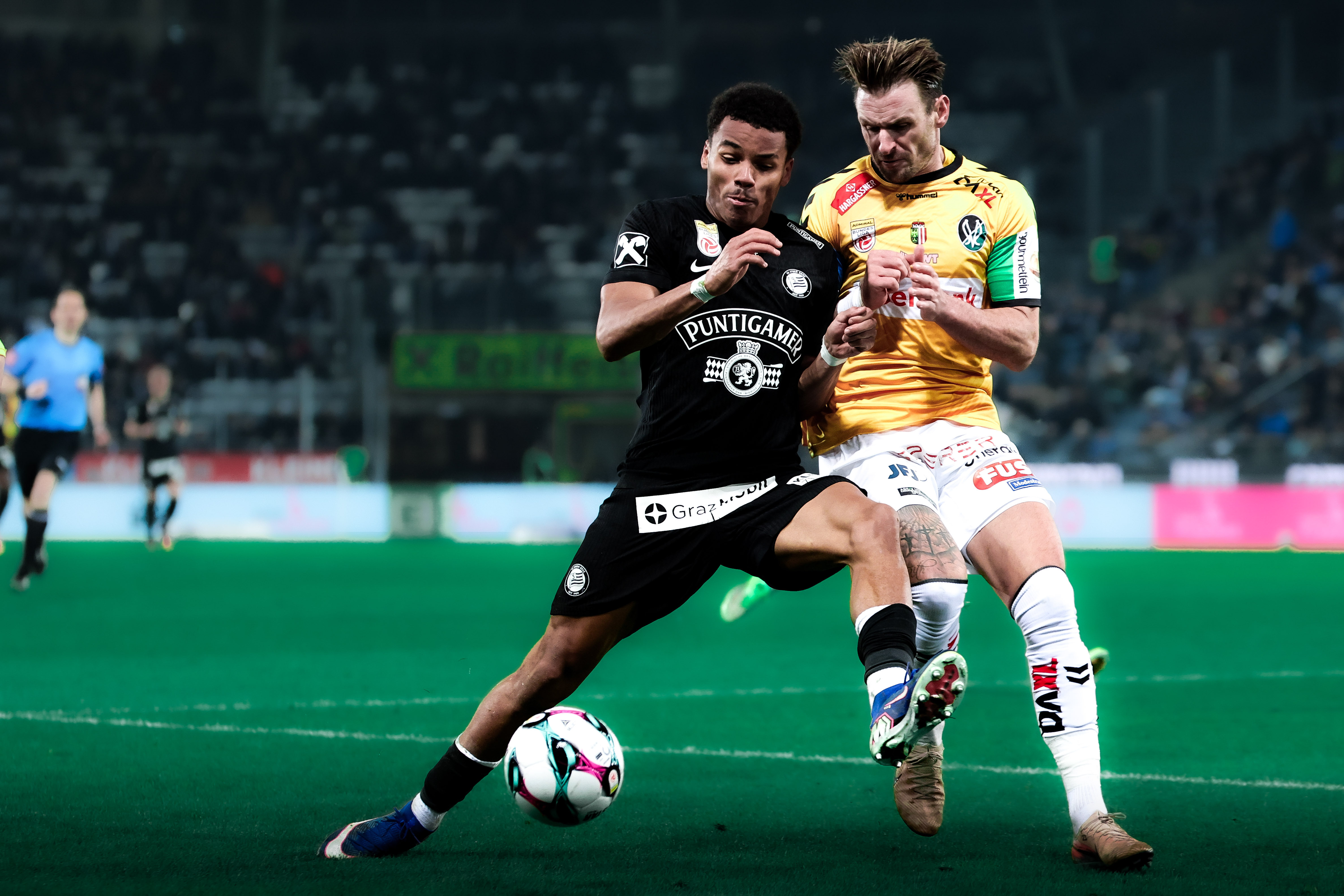 Ein Spieler im schwarzen Trikot und ein Spieler im gelben Trikot kämpfen um einen weißen Ball