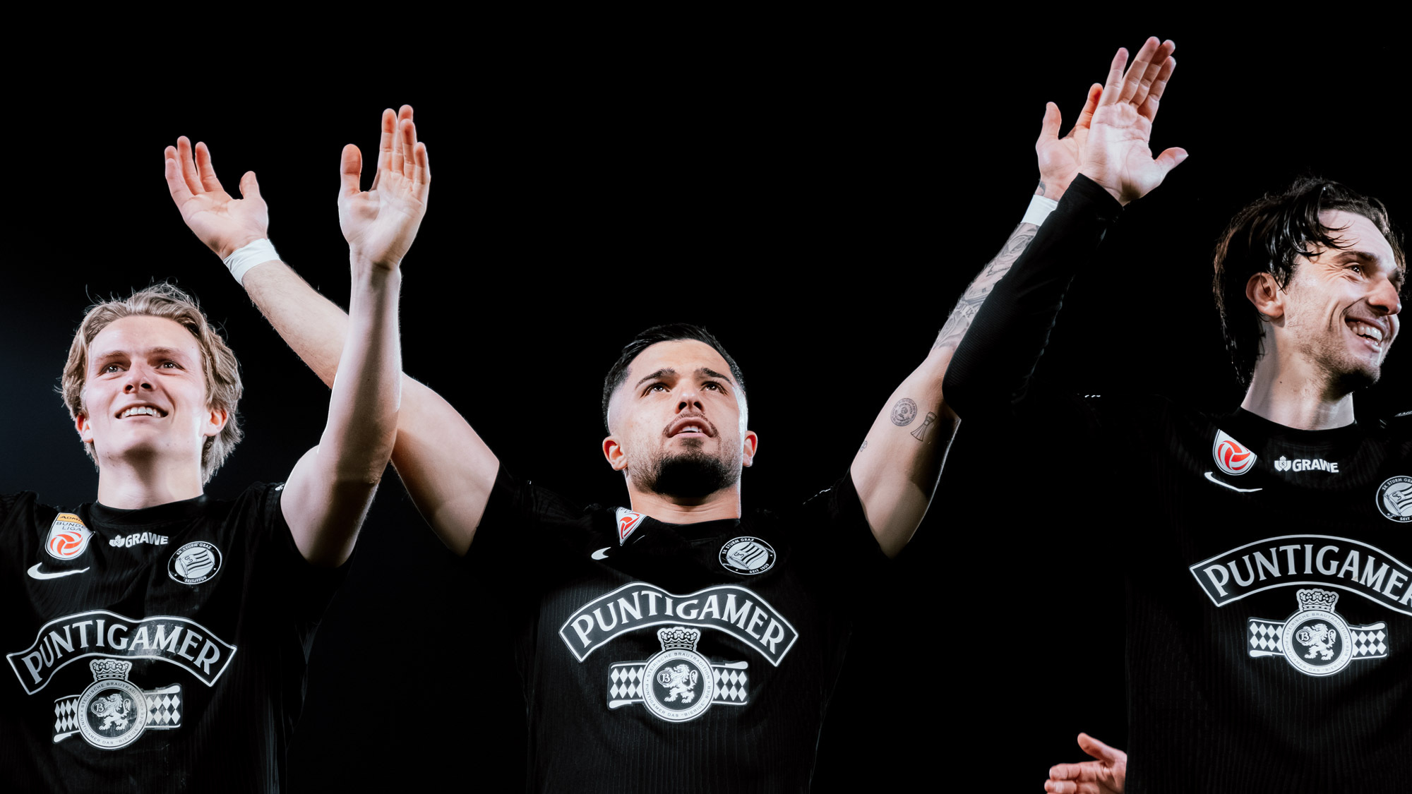 Drei Spieler in schwarzen Trikots jubeln mit den Händen in die Höhe gestreckt