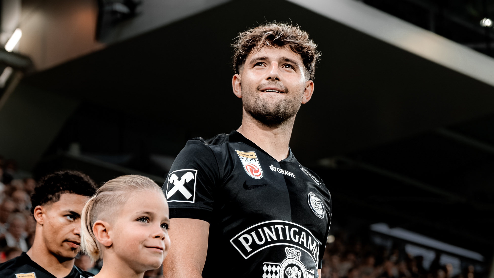 Ein Spieler in einem schwarzen Trikot geht auf's Feld, ein Kind geht mit ihm mit
