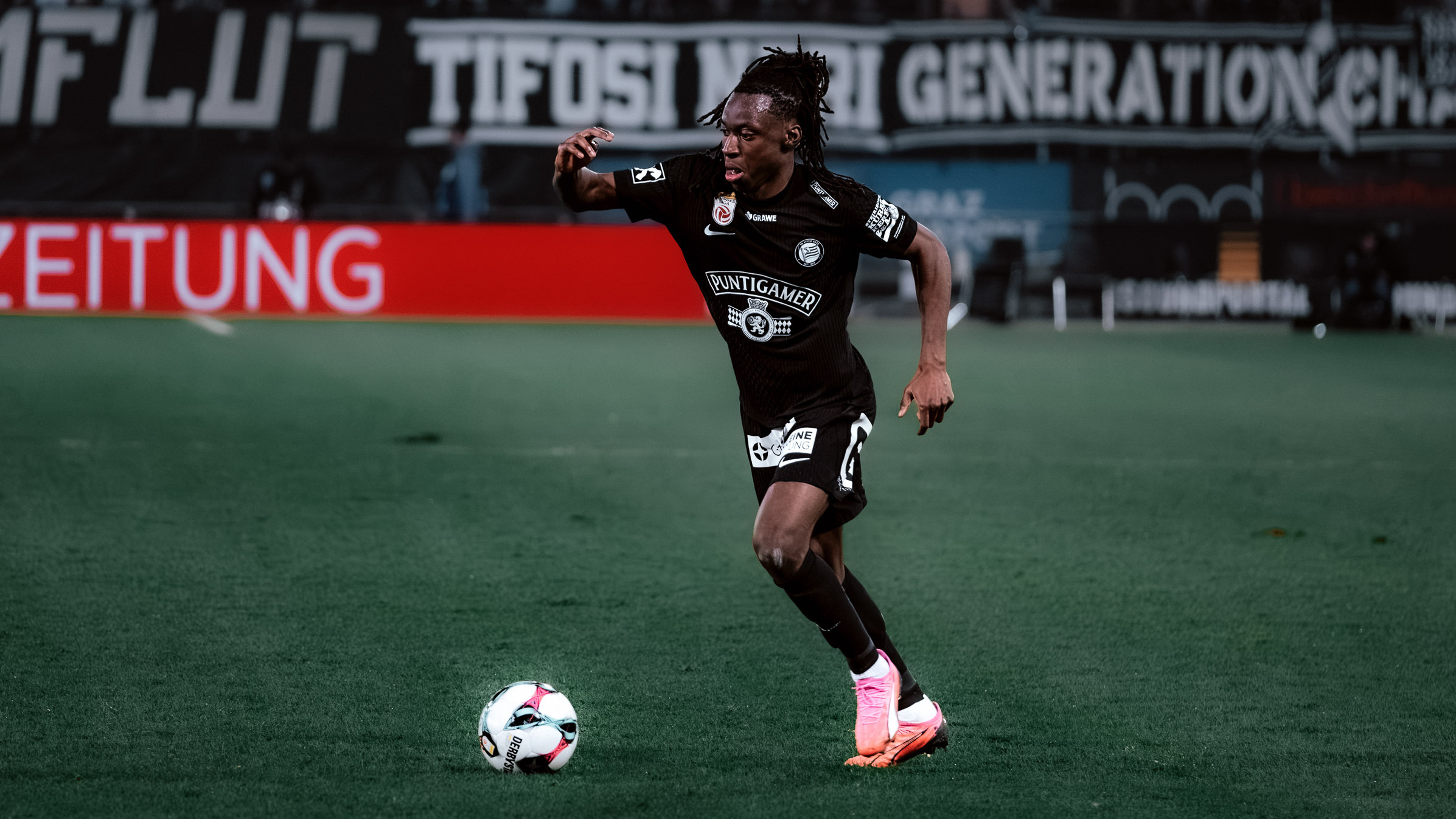 Ein Spieler mit Ball am Fuß trägt ein schwarzes Trikot und eine schwarze Hose