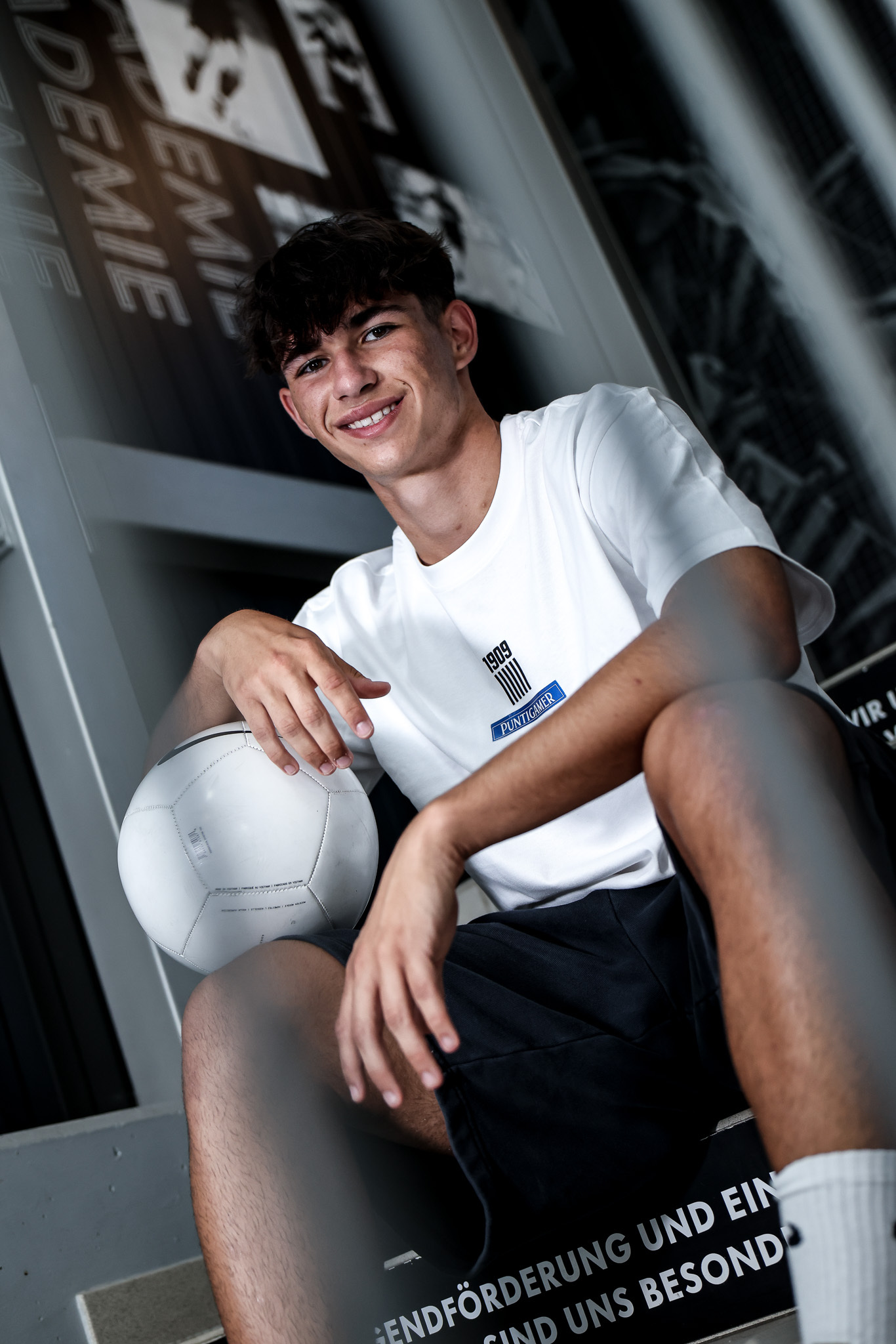 Ein Mann im weißen Shirt sitzt mit Ball auf einer Treppe