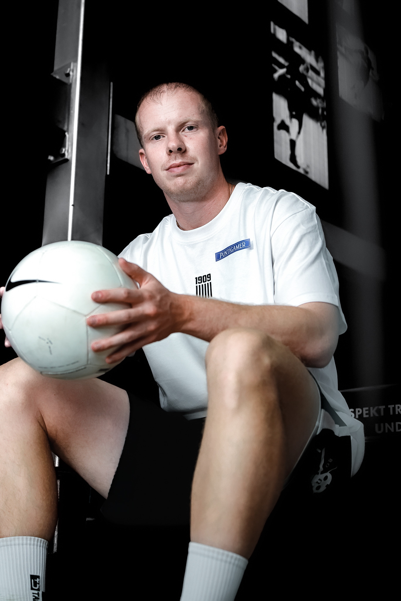 Ein Mann im weißen Shirt sitzt im Stiegenhaus und hält einen weißen Nike Ball in der Hand