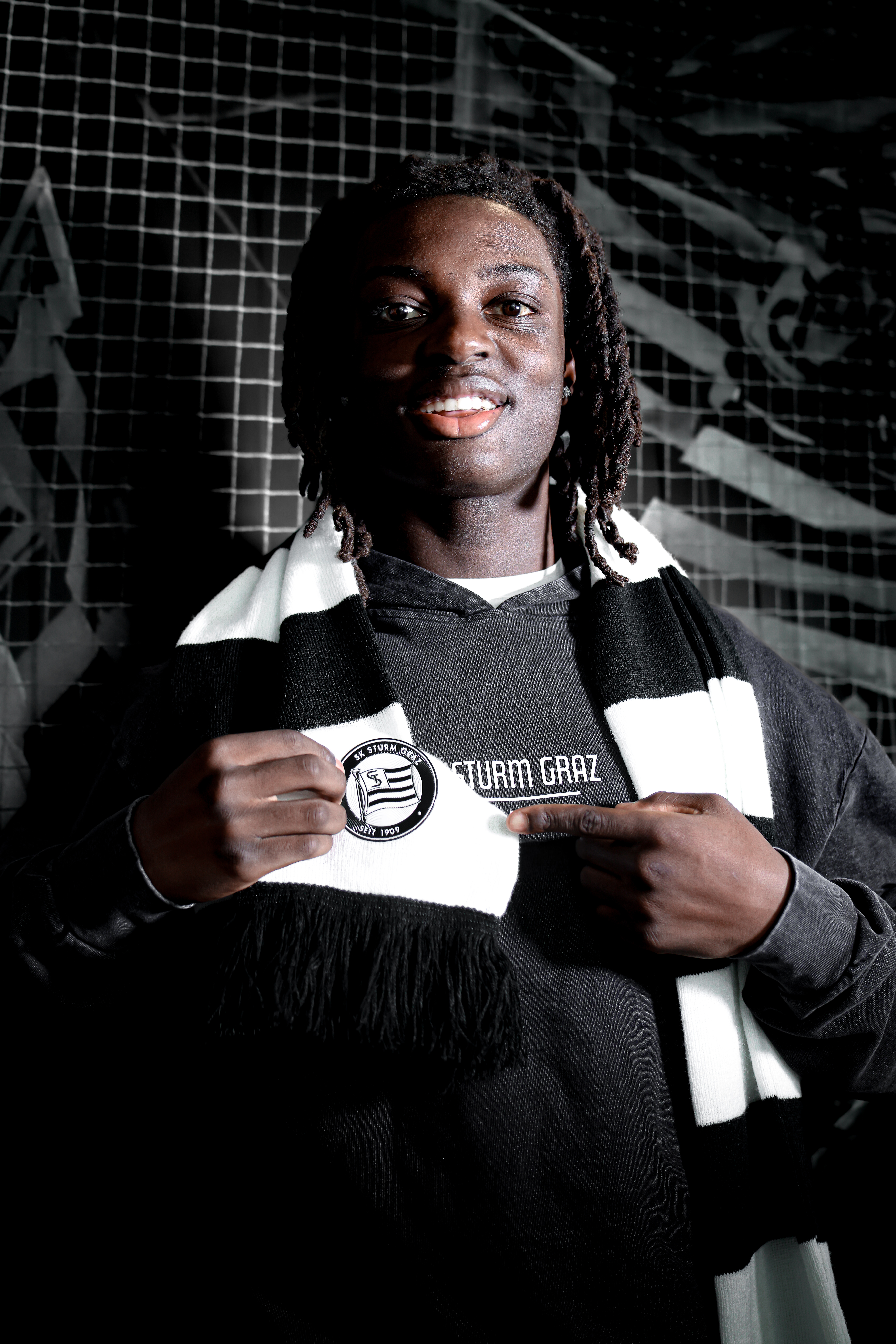 Mann mit schwarz-weißem Schal zeigt auf SK Sturm-Logo.