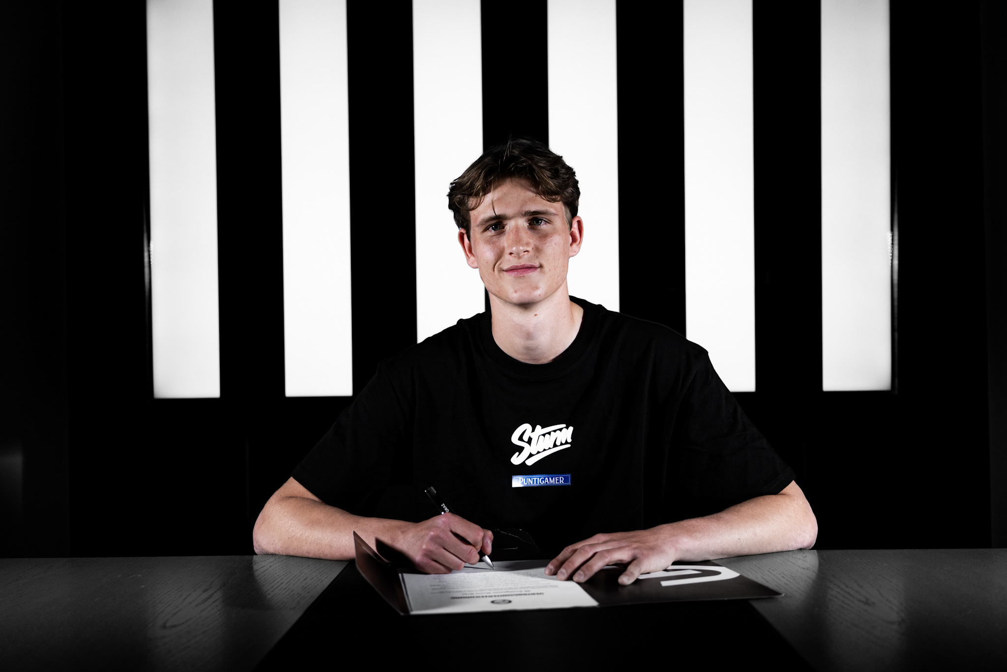 Junger Mann in schwarzem Shirt unterschreibt einen Vertrag.