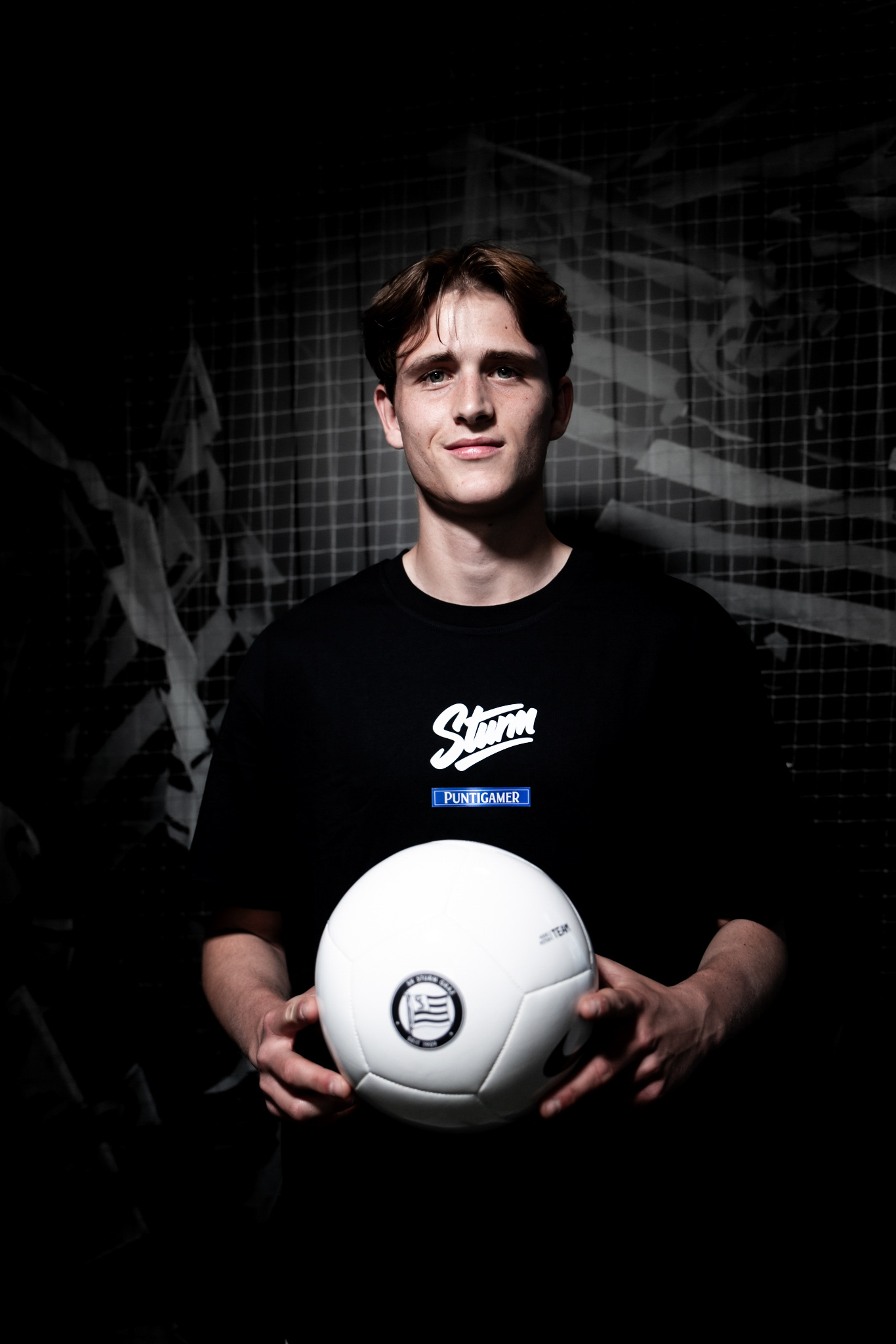 Junger Mann in schwarzem Shirt hält einen weißen Ball.