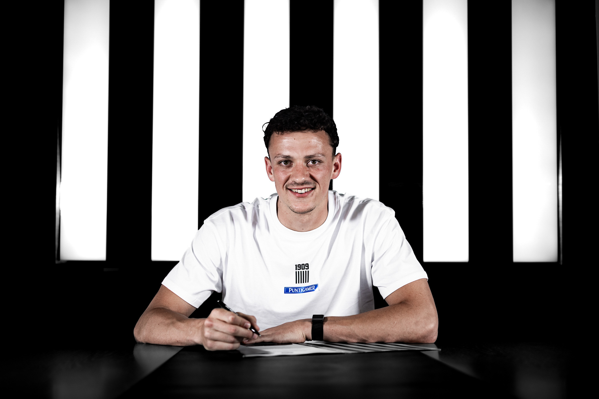 Junger Mann in weißem Shirt unterschreibt einen Vertrag.