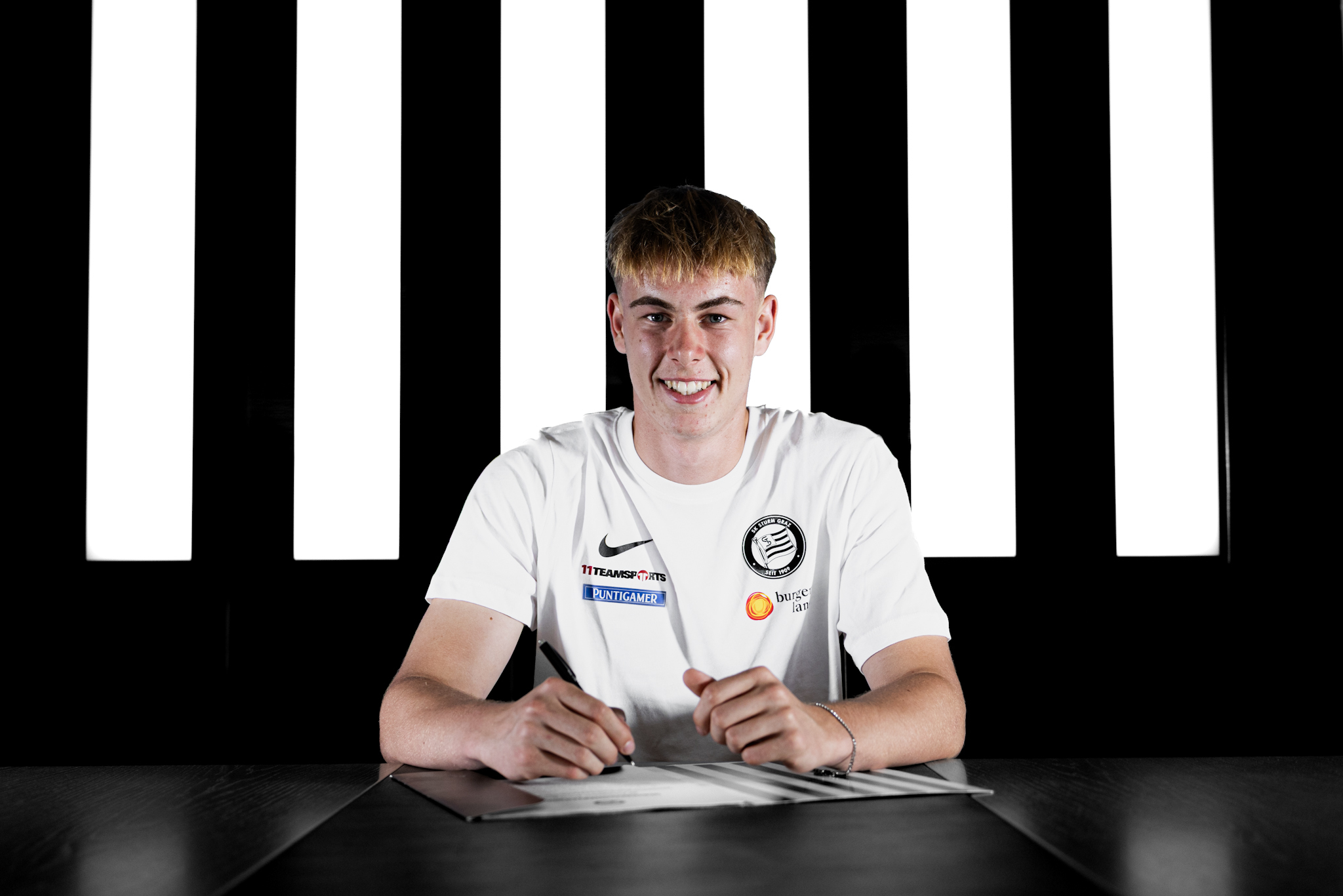 Junger Mann in weißem Shirt unterschreibt einen Vertrag.
