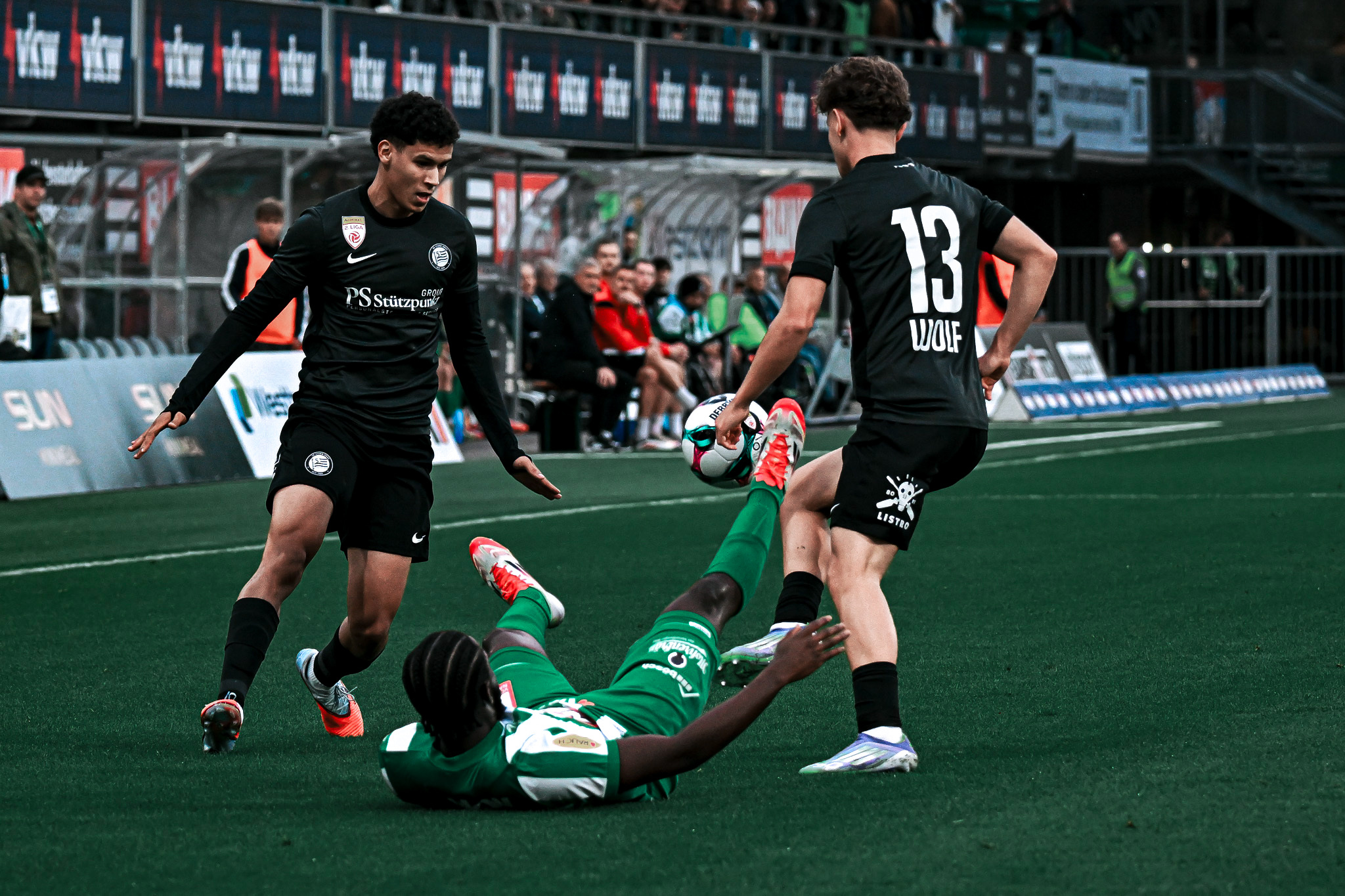 Drei Männer spielen Fußball, einer liegt am Boden.