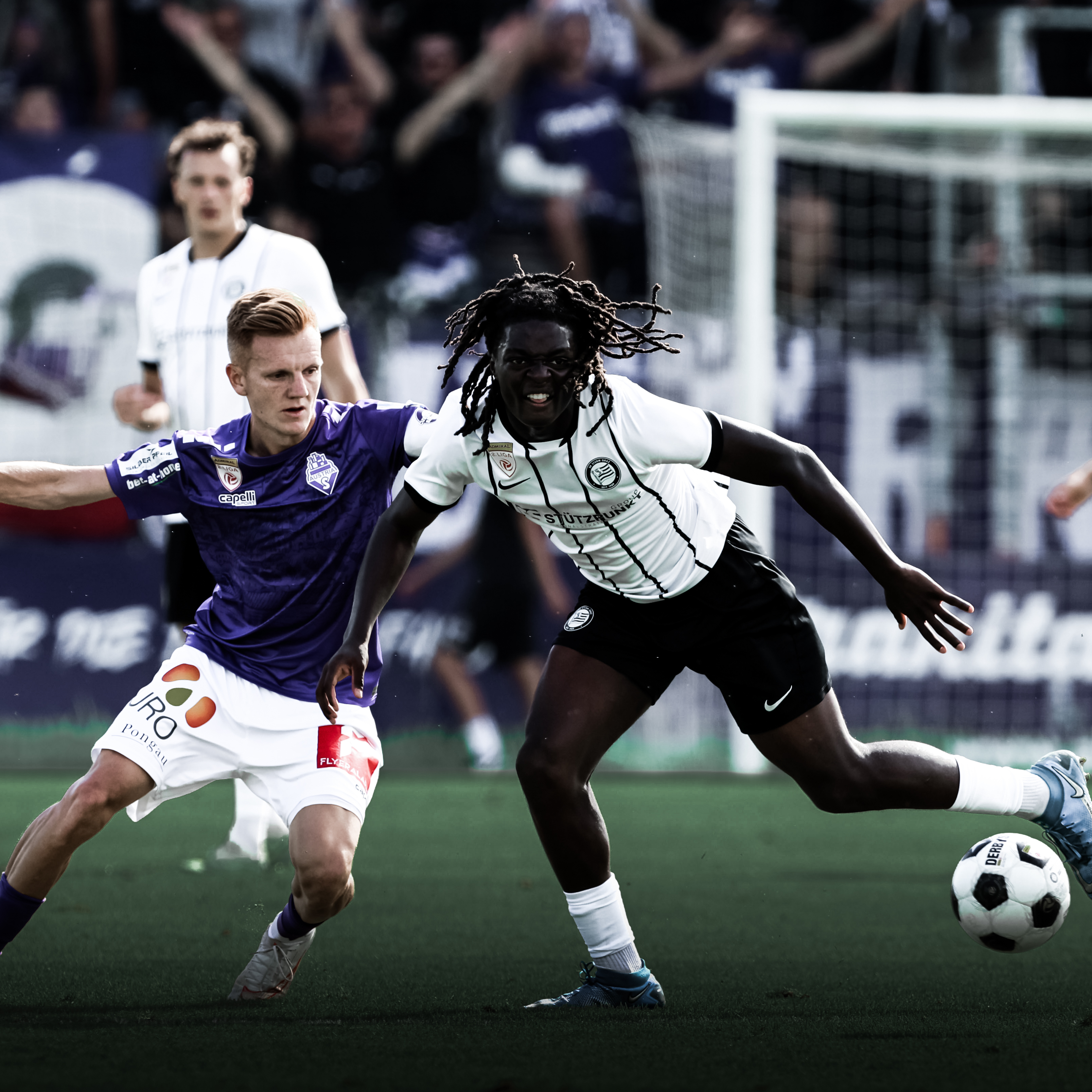 Ein Spieler in einem weißen Trikot kämpft mit einem Spieler in violett um einen weißen Ball.